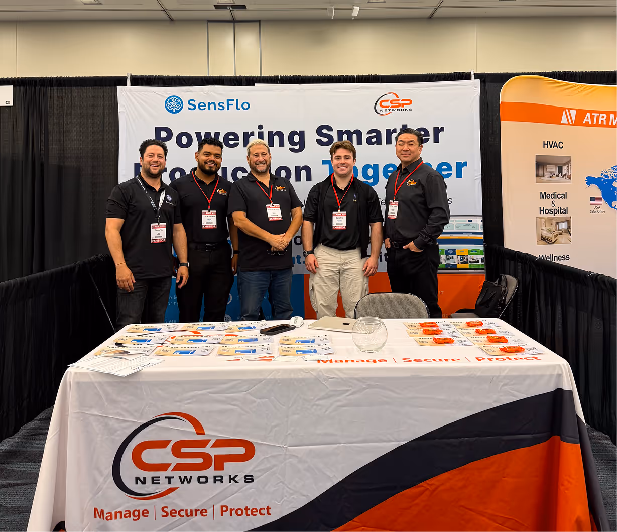 Five men standing behind a CSP Networks booth table with promotional materials at an event.