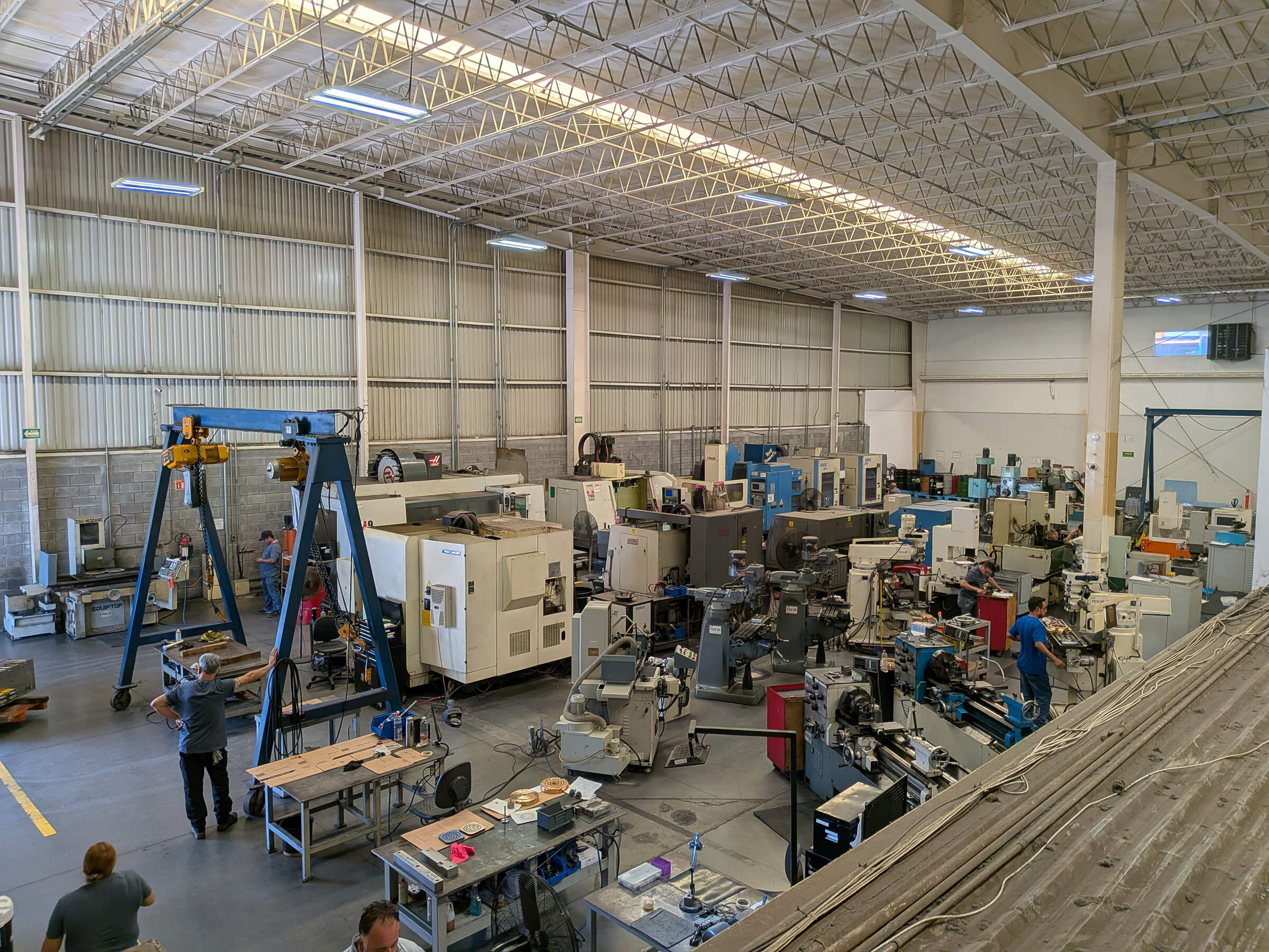 Piso de taller con fresadoras CNC, tornos, equipos de maquinado convencionales y operadores en producción.
