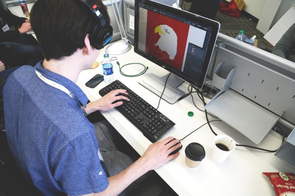 Graphic designer working on digital illustration with headphones using computer and design software in modern office.