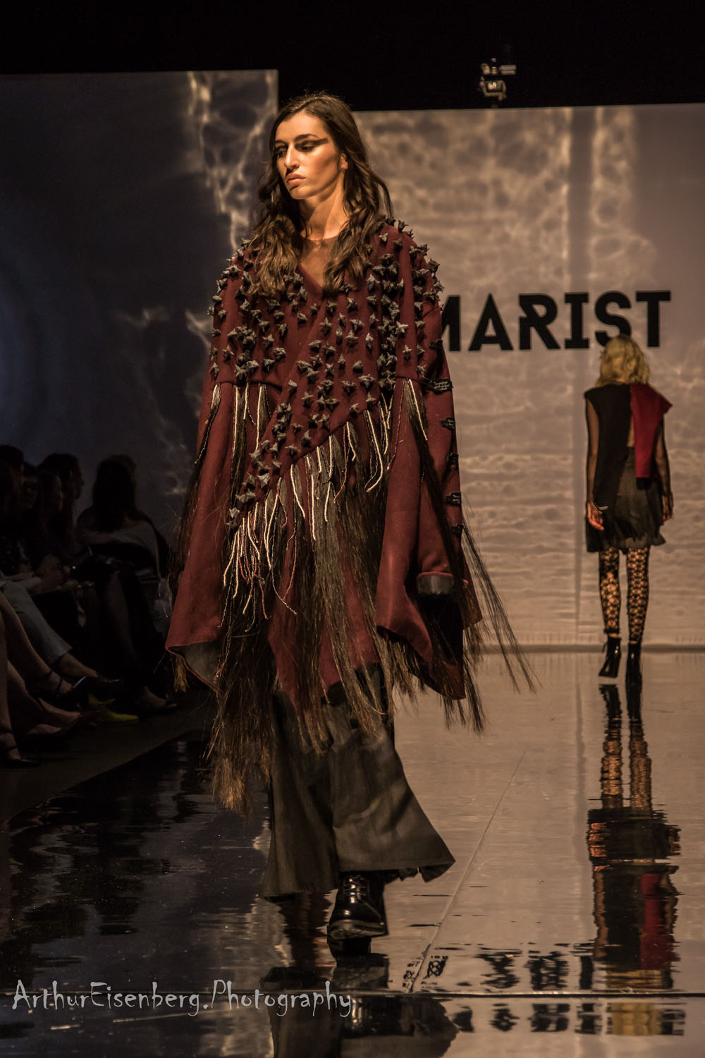 Fashion model walking the runway in an avant-garde outfit with layered textures and fringes at Marist fashion show – career opportunities in fashion design.