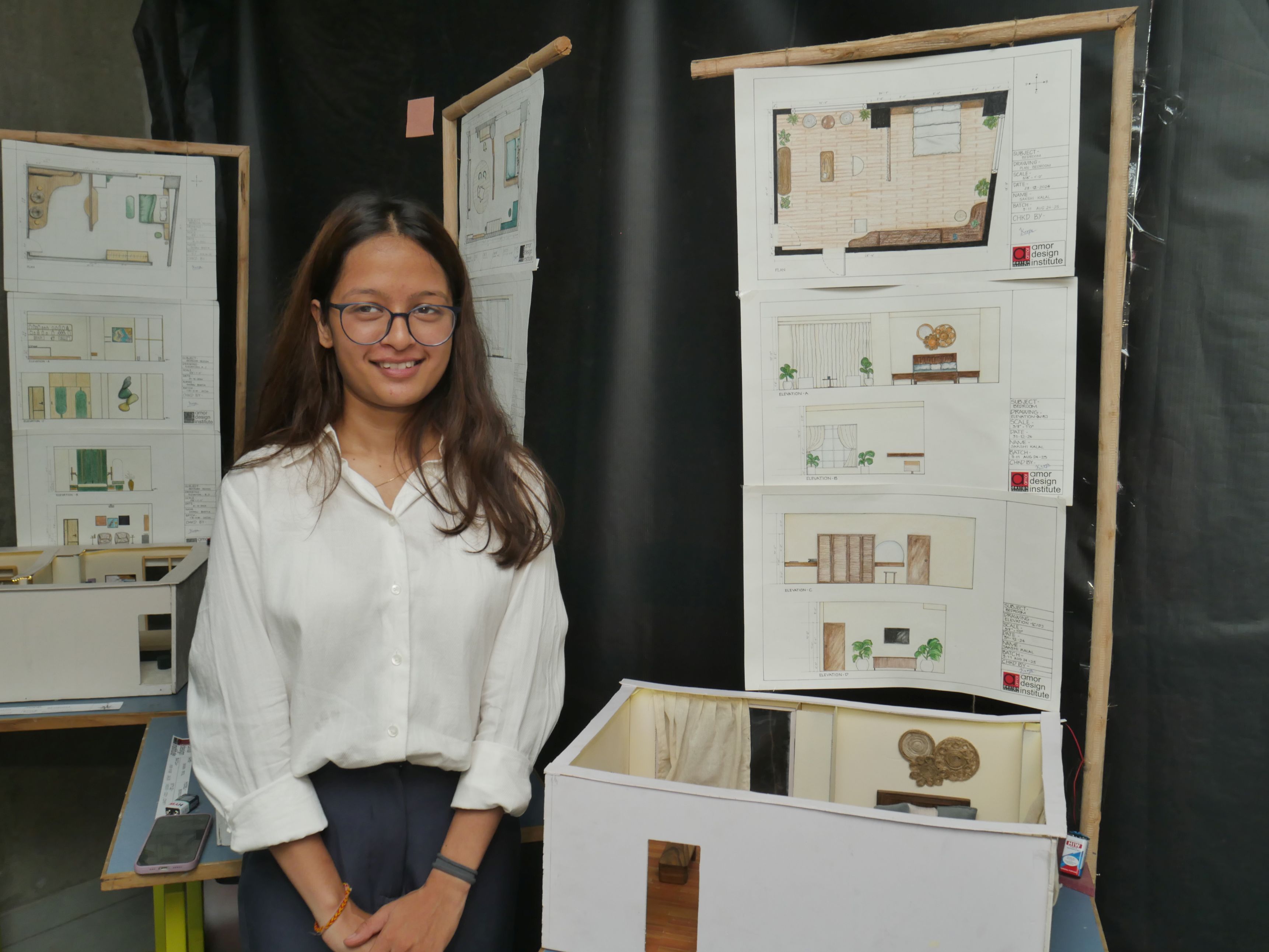Interior design student presenting hand-drawn elevation drawings and room scale model at Amor Rasa annual design exhibition in Ahmedabad