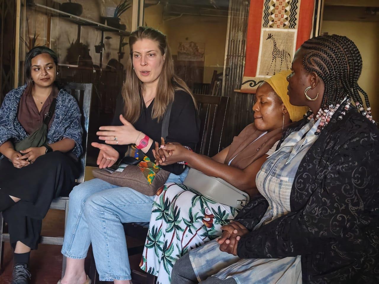 The image shows a group of people engaged in a conversation, sitting in a warm, inviting room with vibrant patterns on the walls.AI-generated content may be incorrect.