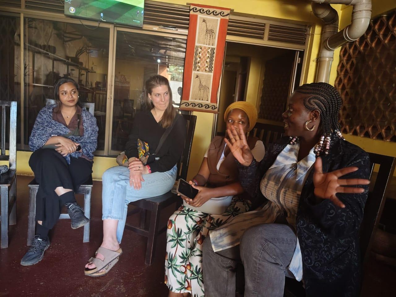 The image shows four people sitting and conversing in a cozy, culturally decorated room.AI-generated content may be incorrect.