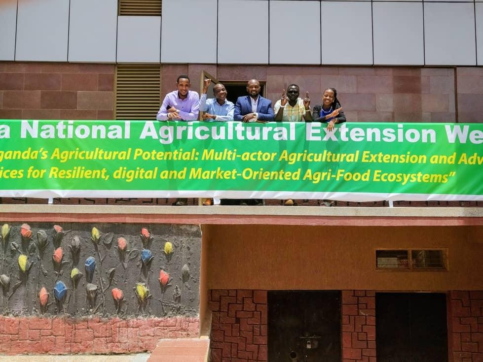 The image depicts a group of people standing in front of a building with a sign promoting multi-actor agricultural extension and support for resilient, digital, and market-oriented agricultural ecosystems.AI-generated content may be incorrect.