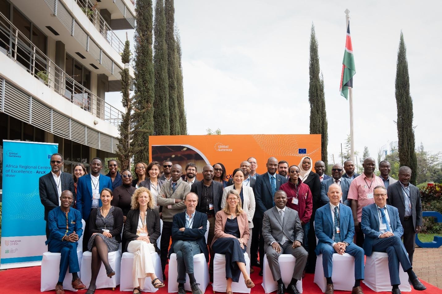 The image depicts a group of people gathered in front of a backdrop featuring the European Union's flag, possibly at an event or conference, with a focus on water and assistance themes.AI-generated content may be incorrect.