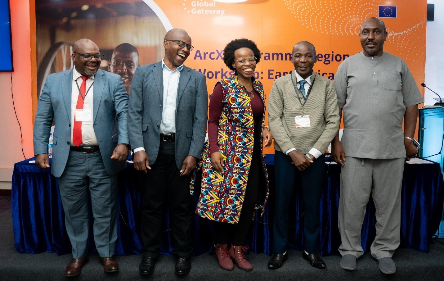 The image shows a group of individuals dressed in formal attire, standing together for a professional or formal event, with the background featuring a patterned design and the logo of an organization or institution.AI-generated content may be incorrect.