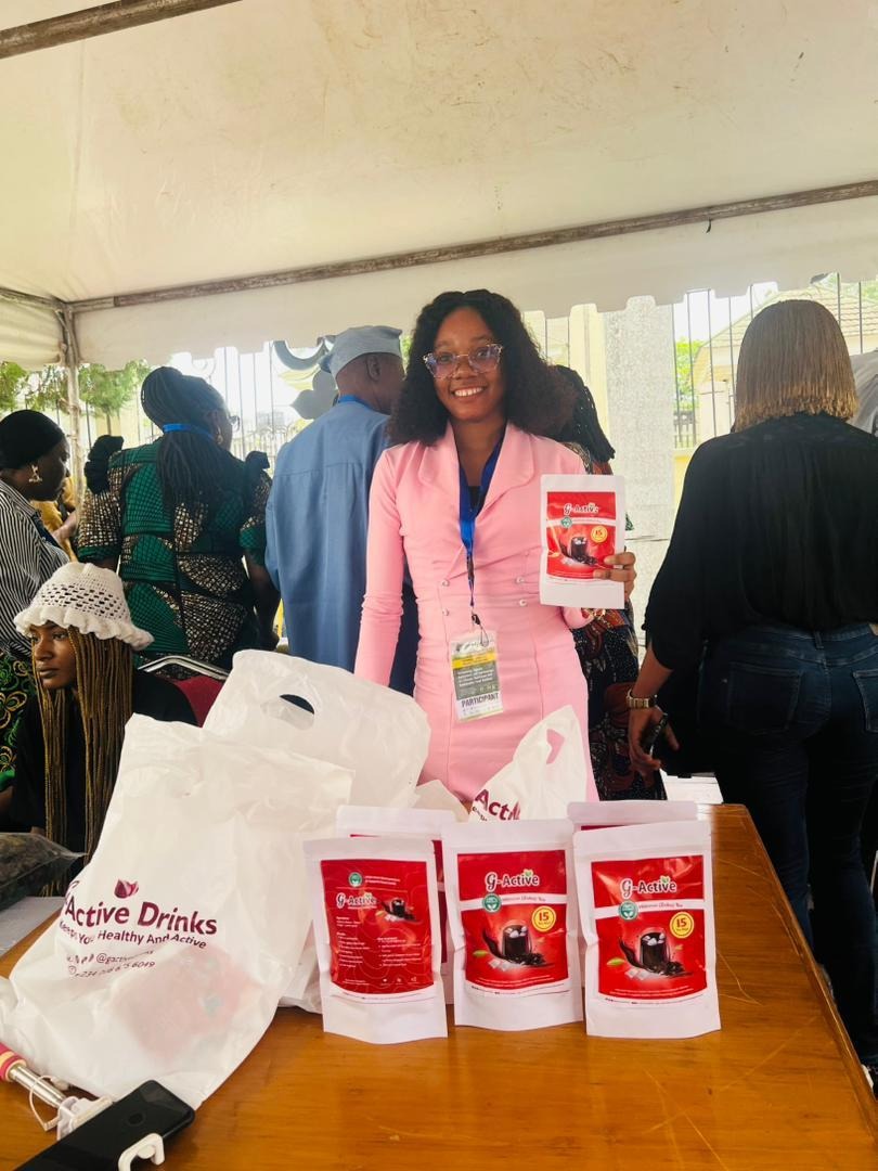 The image shows a person standing at a table under a tent, holding a bag of g-Active drinks and surrounded by other people, possibly at an event.AI-generated content may be incorrect.
