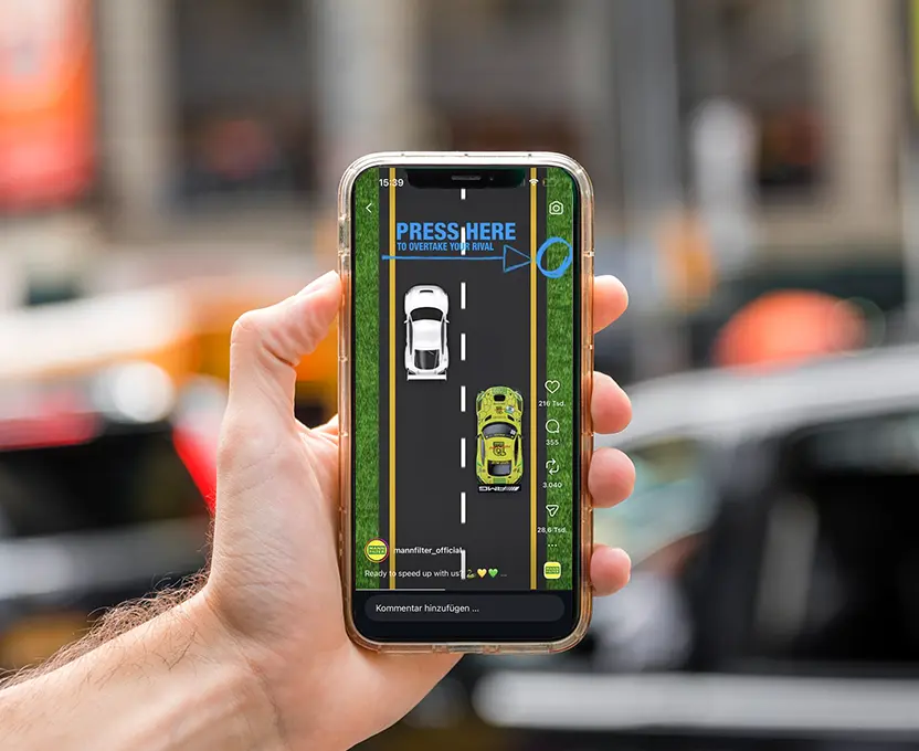 Eine Hand, die ein Smartphone hält, auf dem ein Rennspiel mit zwei Autos auf einer Straße zu sehen ist, sowie die Aufforderung, auf den Bildschirm zu tippen.