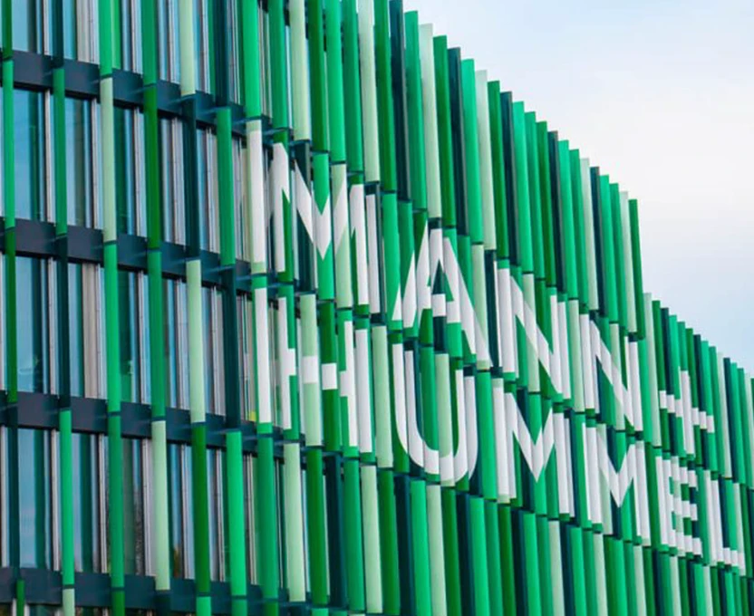 Moderne Gebäudefassade mit begrünten vertikalen Lamellen, auf denen der Schriftzug „MANN+HUMMEL“ zu sehen ist.