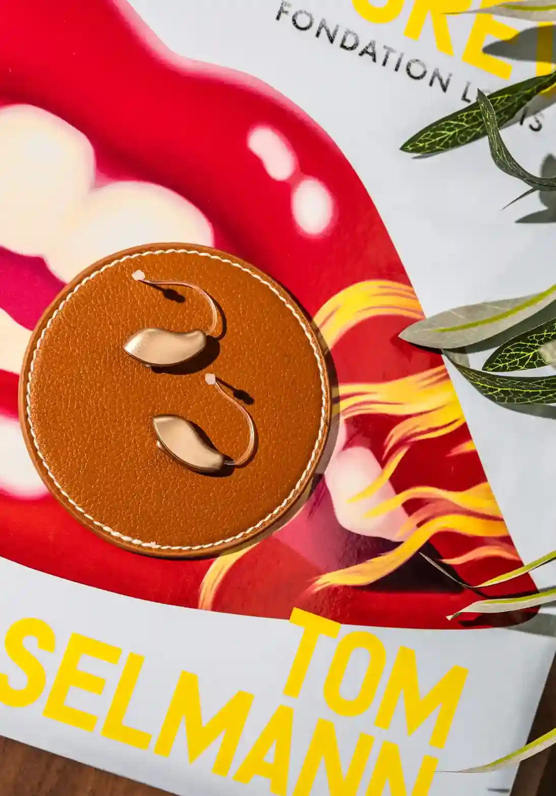 Deux aides auditives dorées posées sur un support en cuir marron, sur une affiche colorée avec du texte jaune et des feuilles vertes à droite.