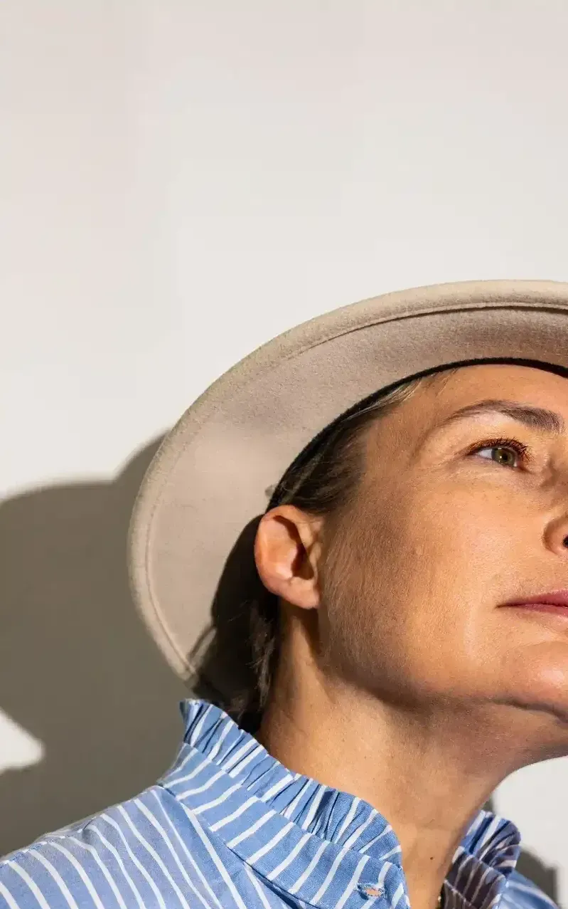 Femme portant un appareil auditif, regarde au loin et porte aussi un chapeau