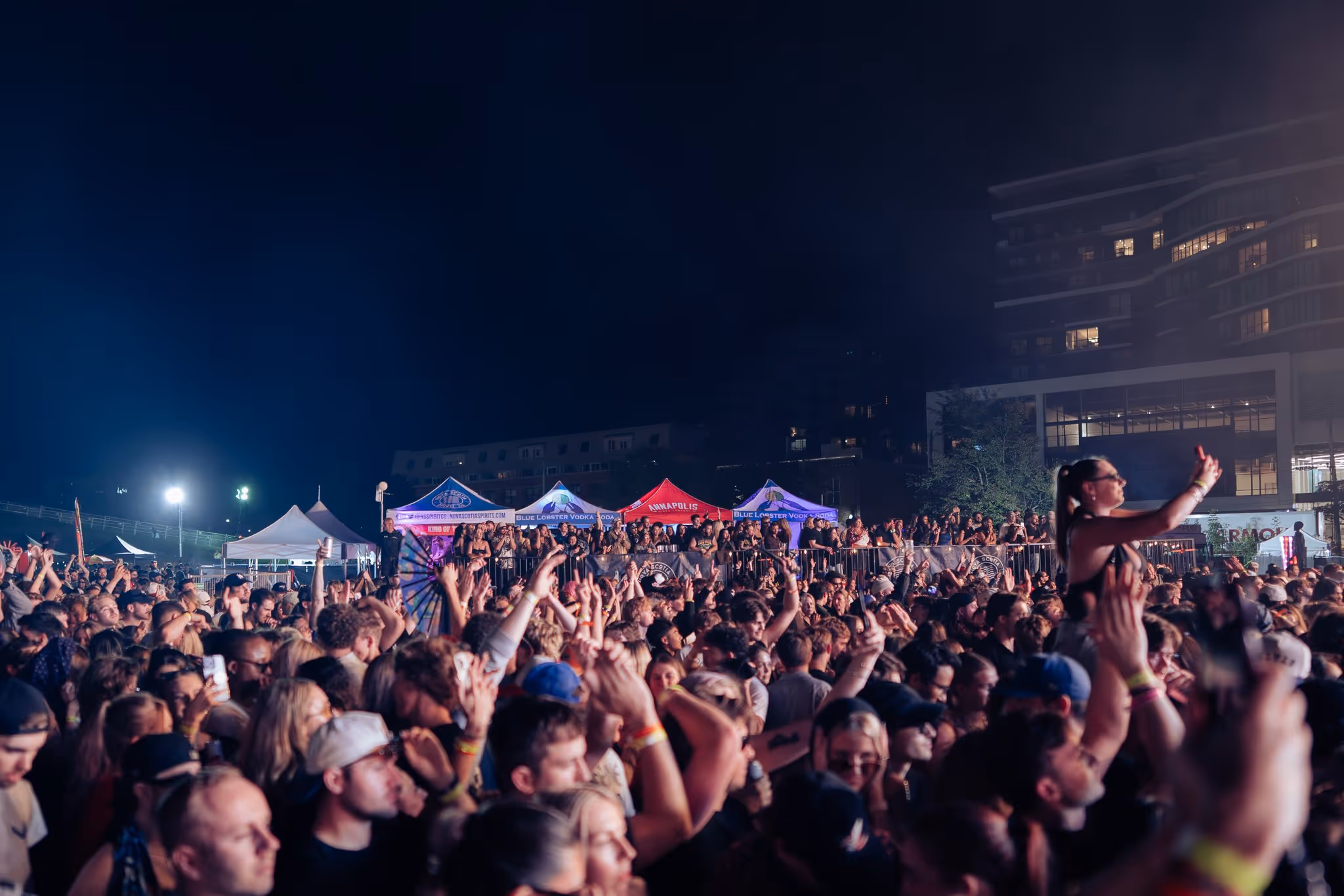Night festival crowd with lit vendor tents and the Halifax skyline behind, Magnetic World Music Festival, Citadel Hill