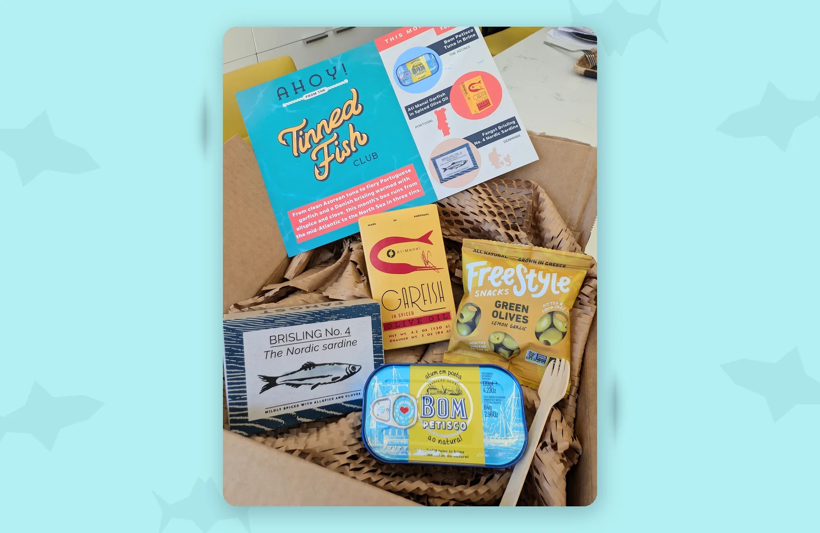 Tinned Fish Club August 2026 box with Bom Petisco tuna, Ati Manel garfish, Fangst Brisling No. 4 and Freestyle green olives