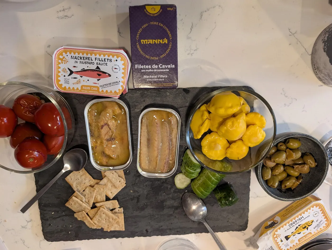Miss Can and Manna mackerel in mustard on a slate board with crackers, tomatoes, cucumber, olives and pickled peppers