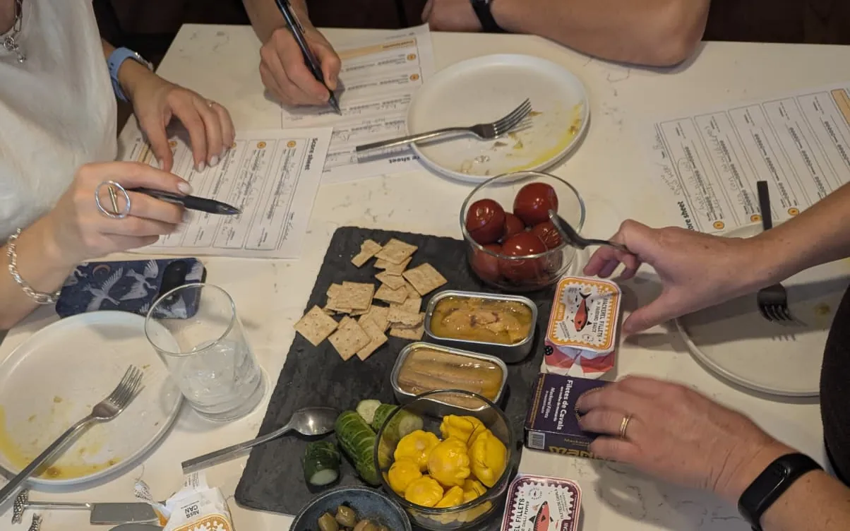 Friends around a table scoring tinned fish on score sheets at a tasting party