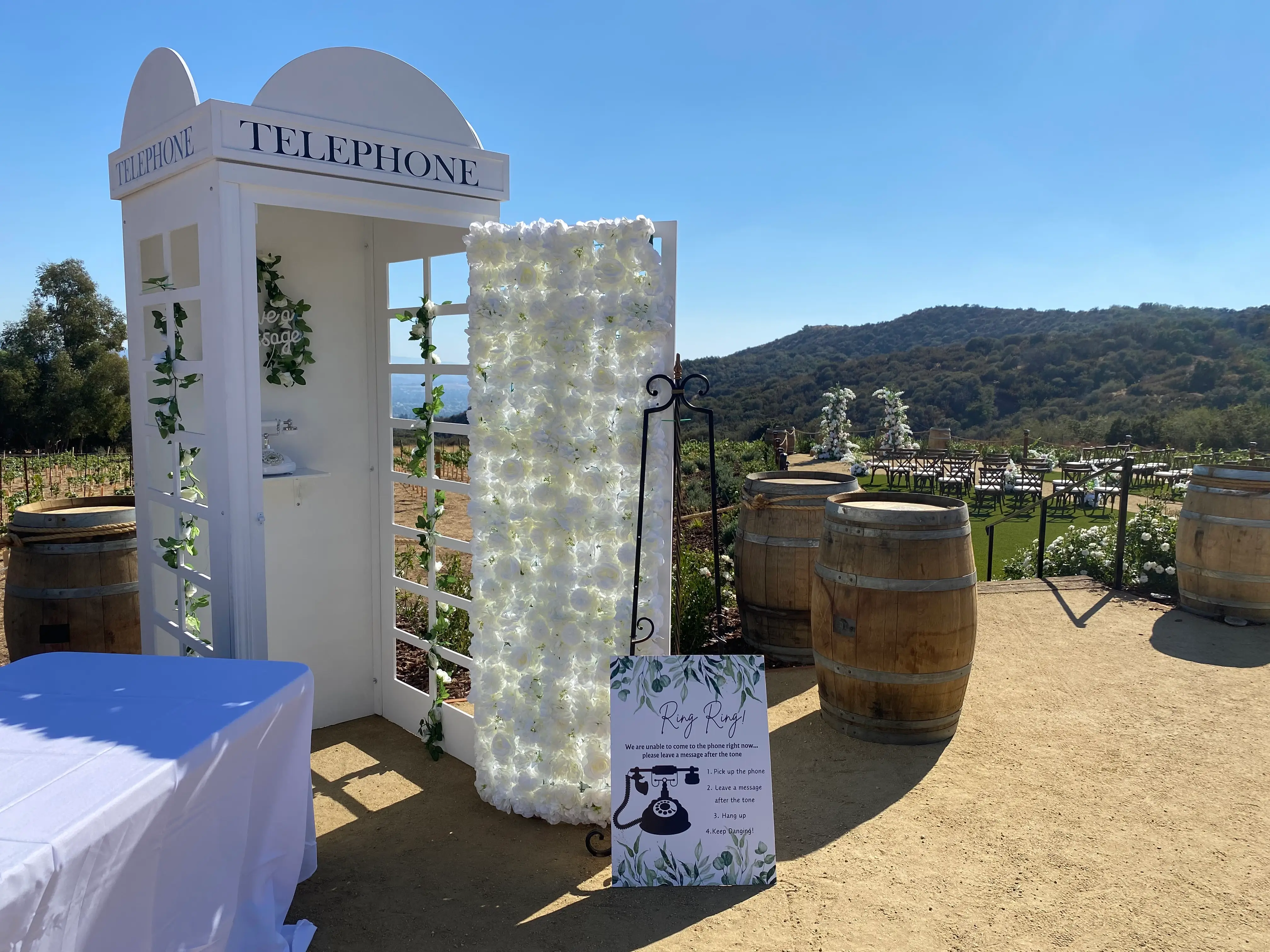 A white phone booth with a sign for leaving voice messages for the bride and groom at their wedding.