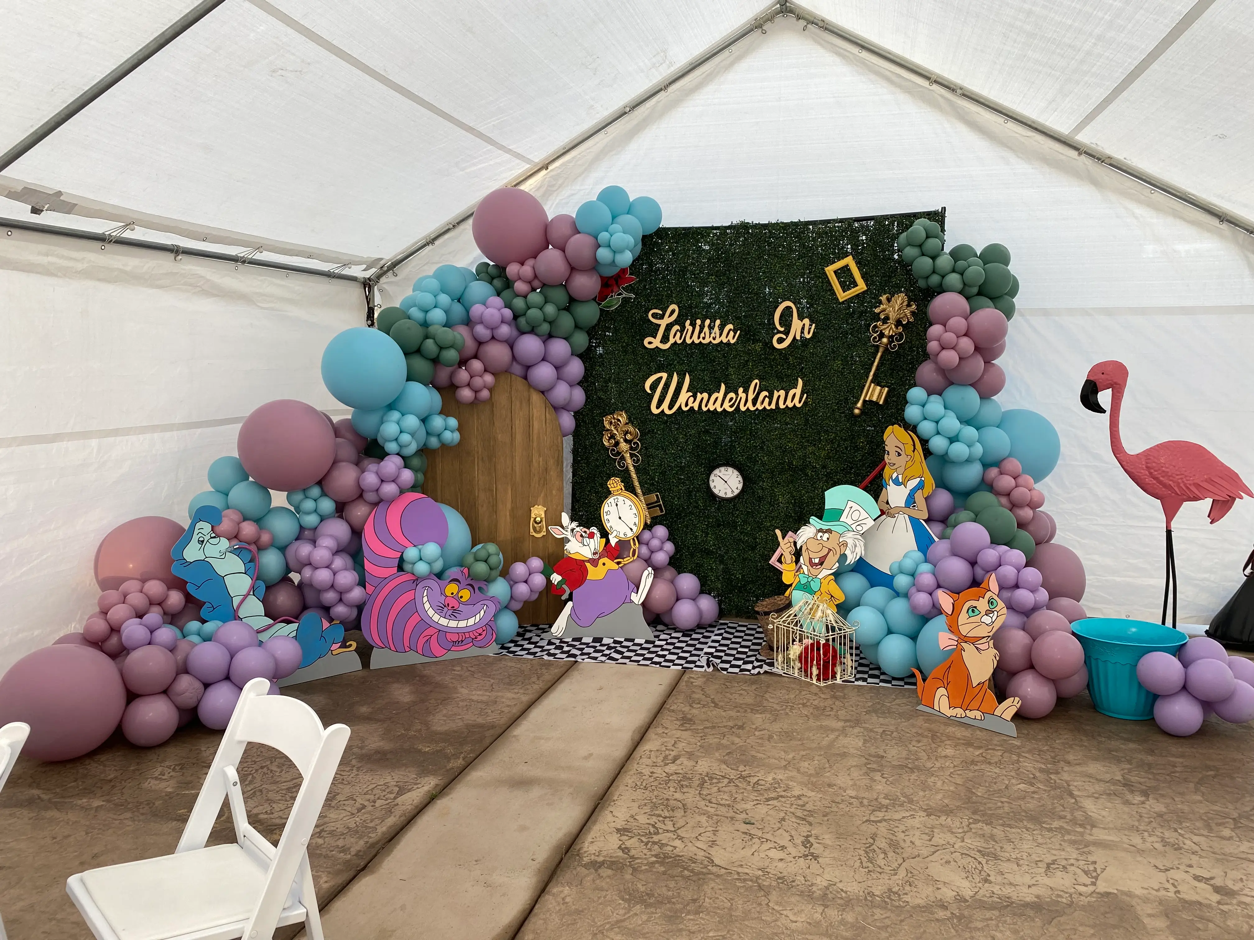 A birthday backdrop adorned with colorful balloons and a sign reading "Larissa In Wonderland," themed for a Wonderland celebration.