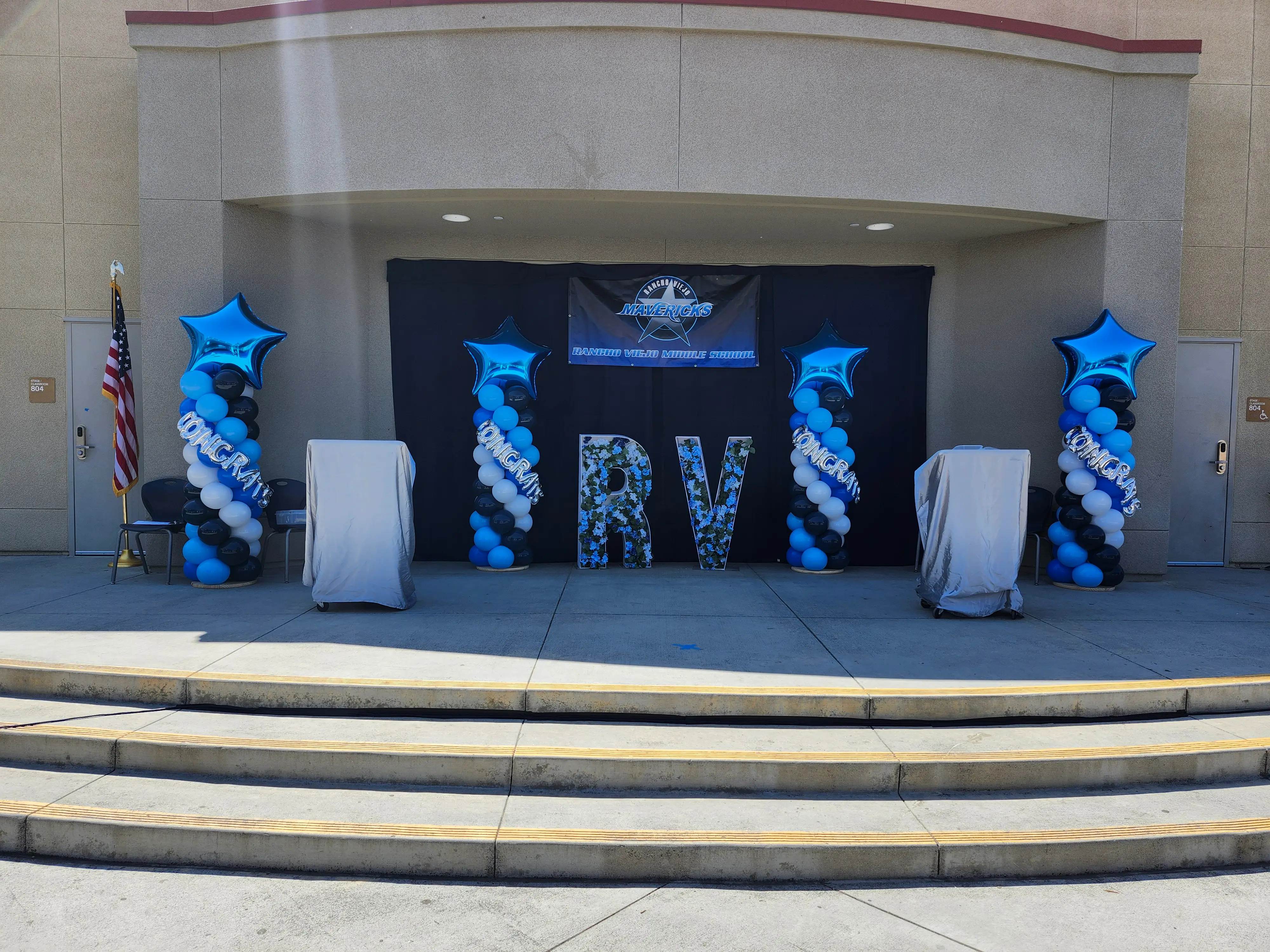 Graduation stage adorned with blue balloons and a prominent sign for the ceremony.