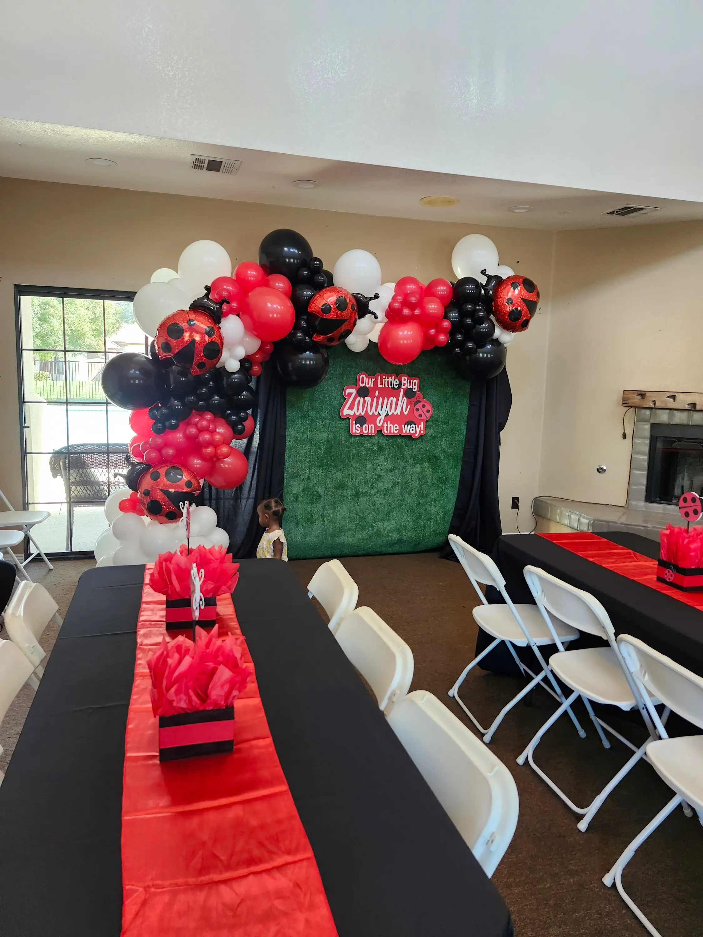 A party room adorned with red and black balloons, featuring a ladybug baby shower backdrop.