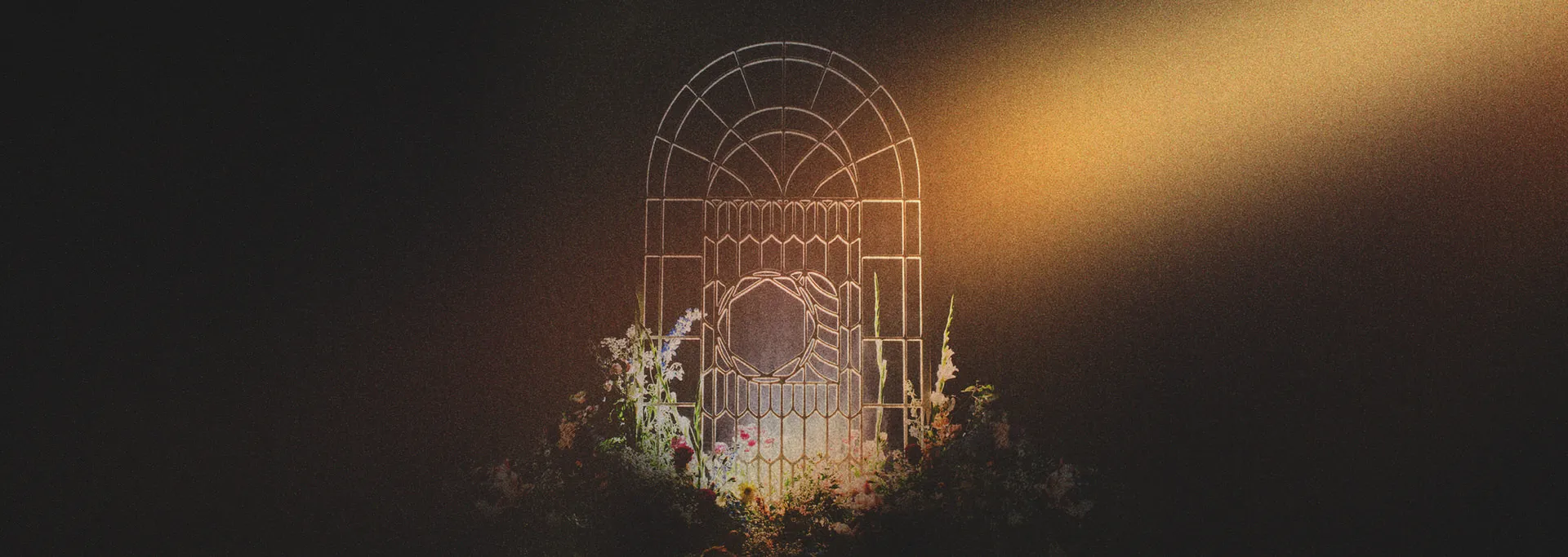 Dimly lit iron gate with floral decorations at its base and a warm light shining from the right.
