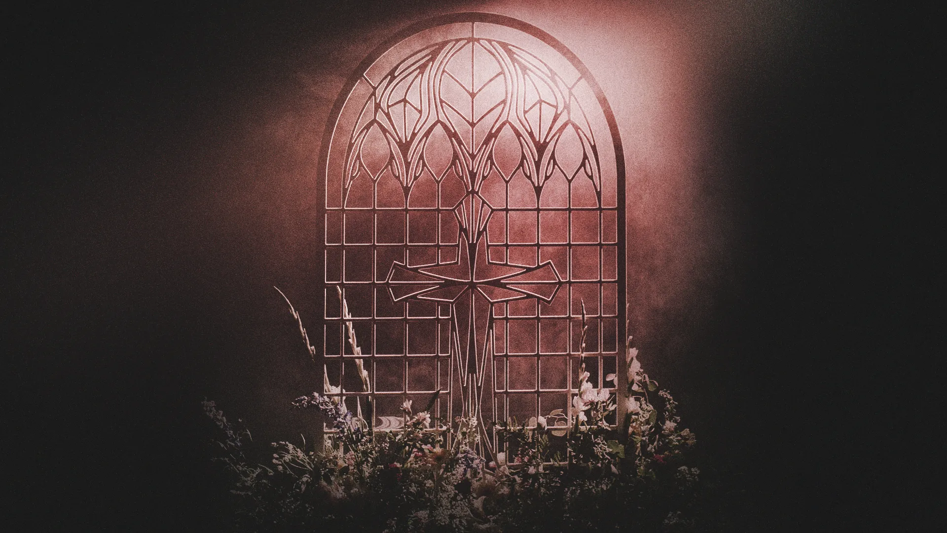 Decorative iron gate with a cross design, illuminated softly with flowers at the base.