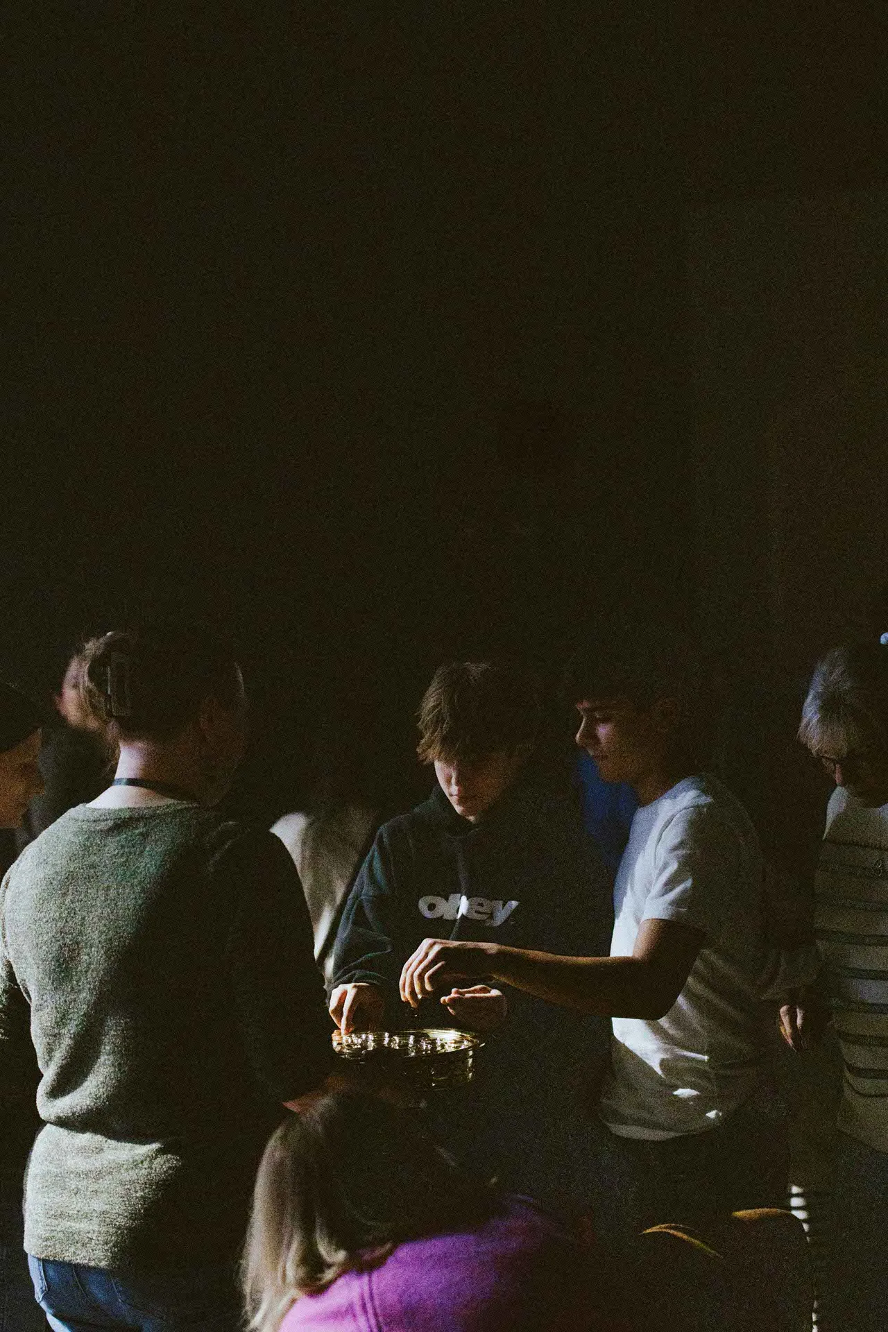 People gathered in dim light passing or receiving communion elements from a golden tray.