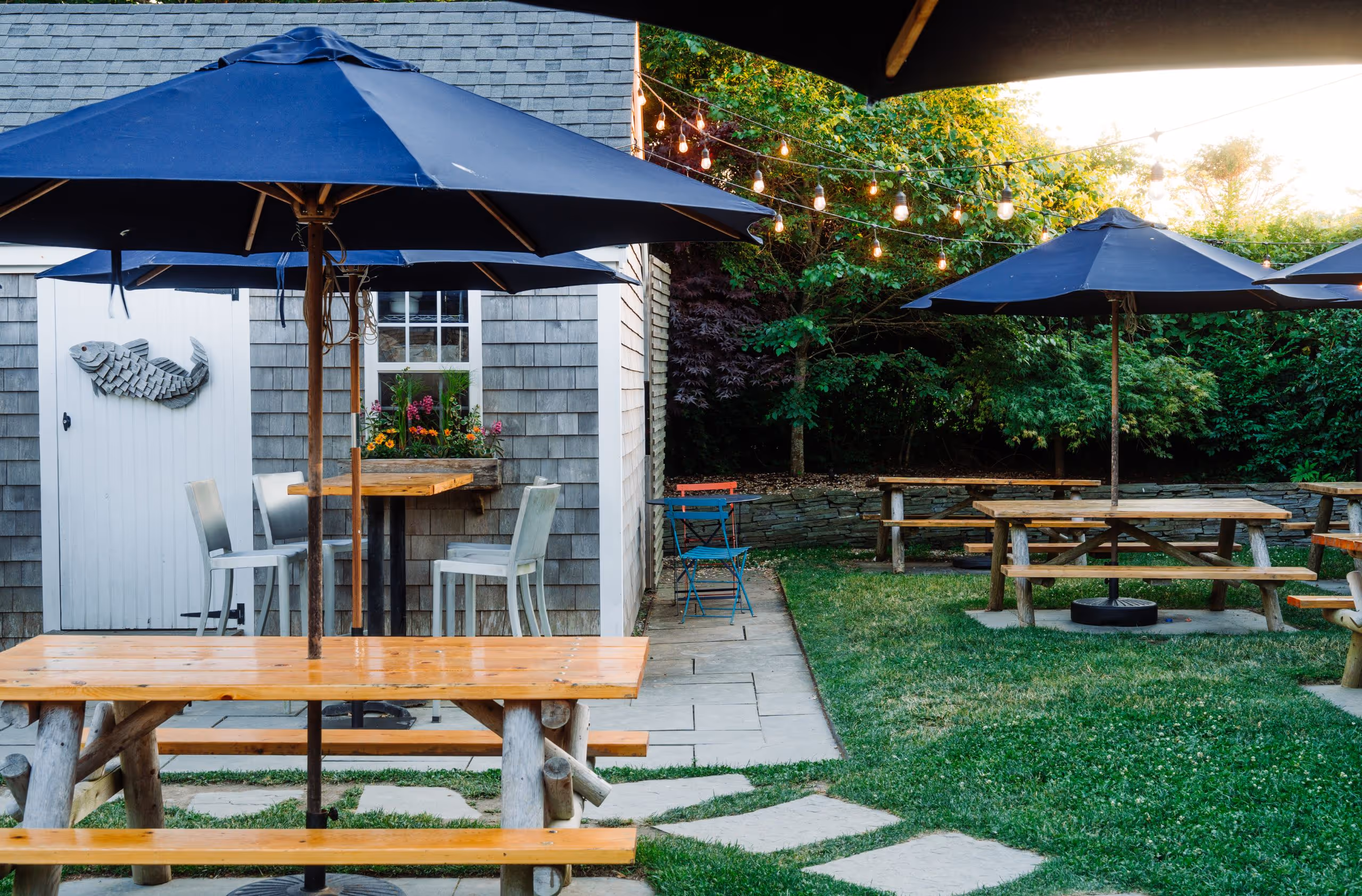 Multiple picnic tables with navy umbrellas in a garden setting at 167 Raw Nantucket.