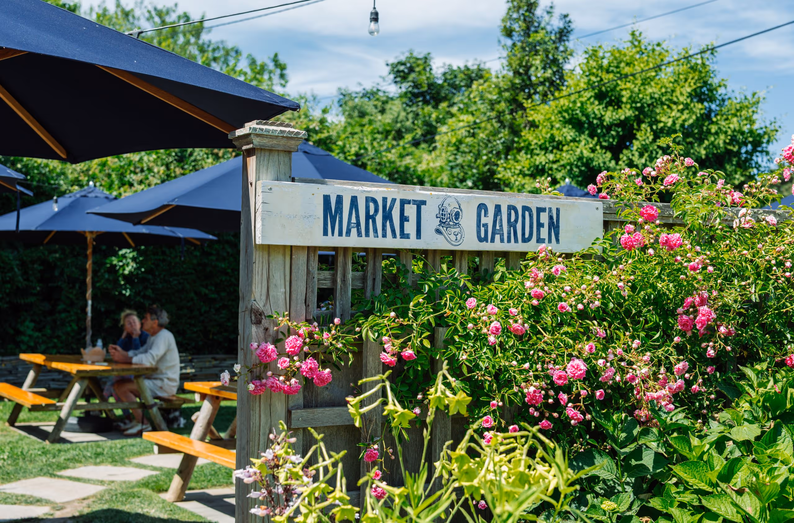 Garden entrance with blooming pink flowers, and people dining in the background at 167 Raw Nantucket.