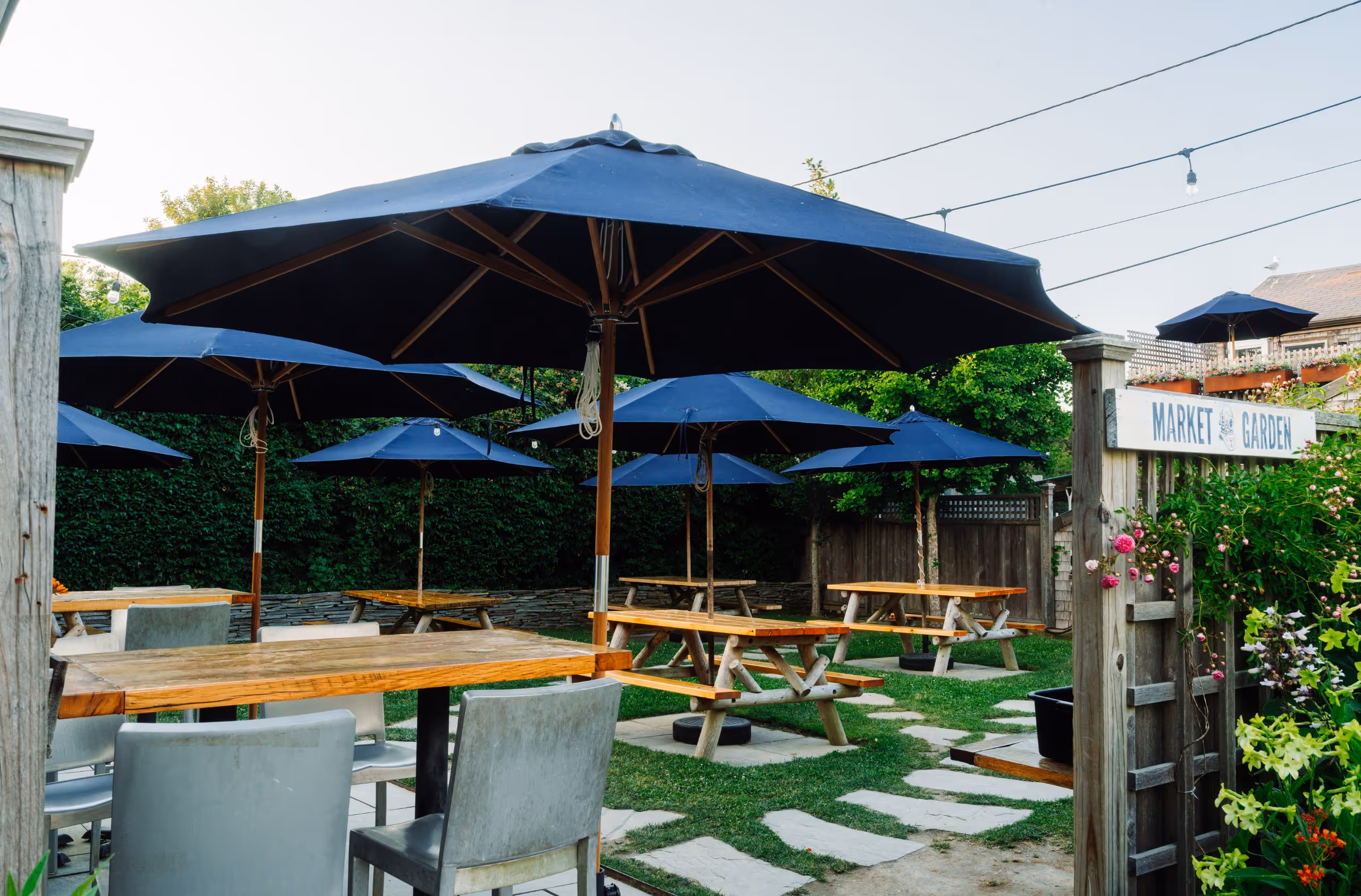 Outdoor dining area with picnic tables, string lights, and blue umbrellas at 167 Raw Nantucket.