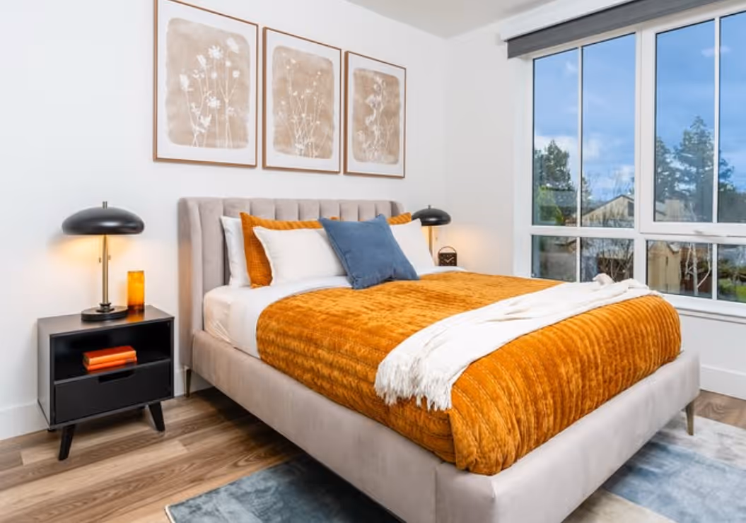 A bedroom with large windows, a bed with orange and white bedding.