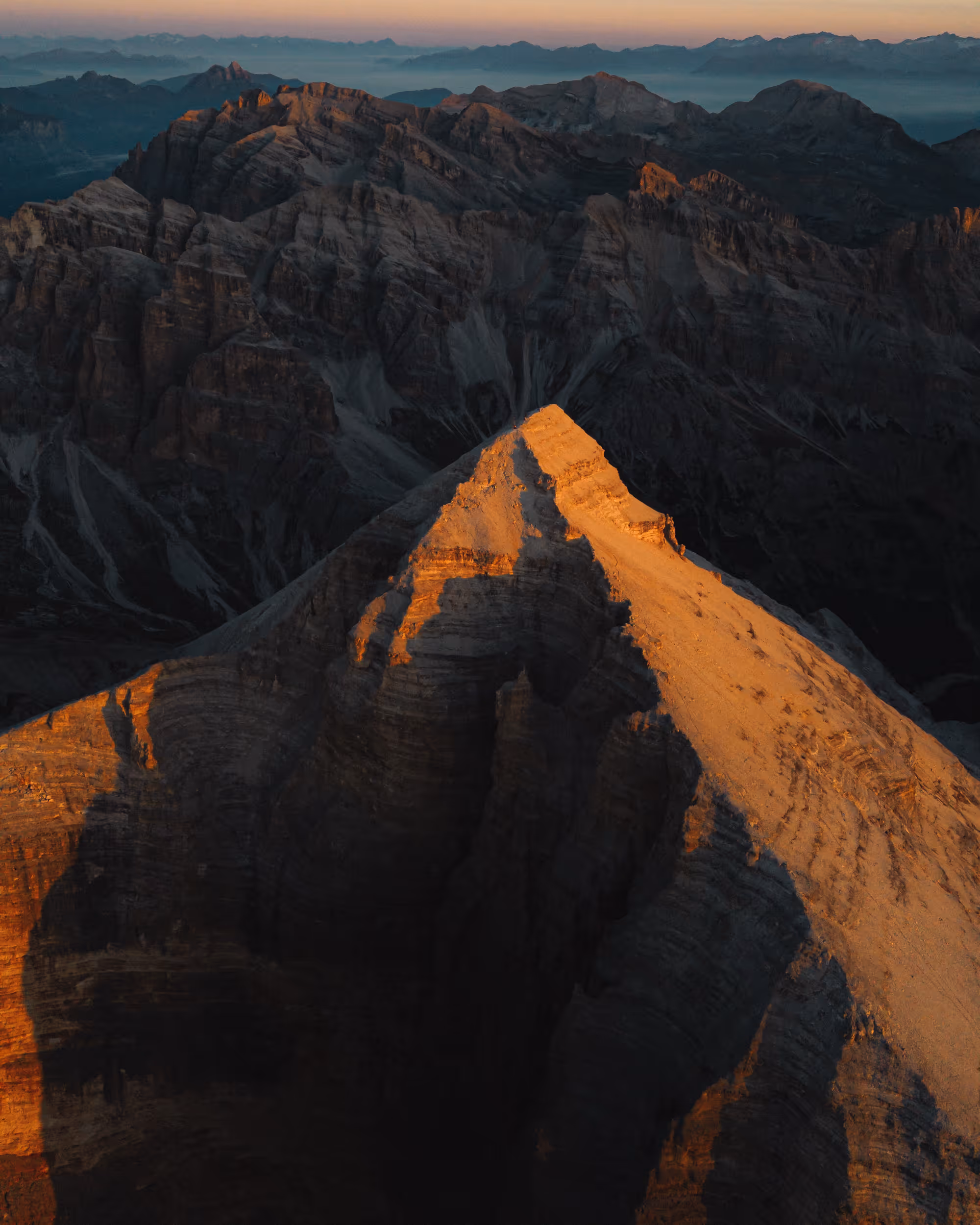 Mountain peak bathed in golden sunlight with surrounding rugged mountains in shadow during sunset.
