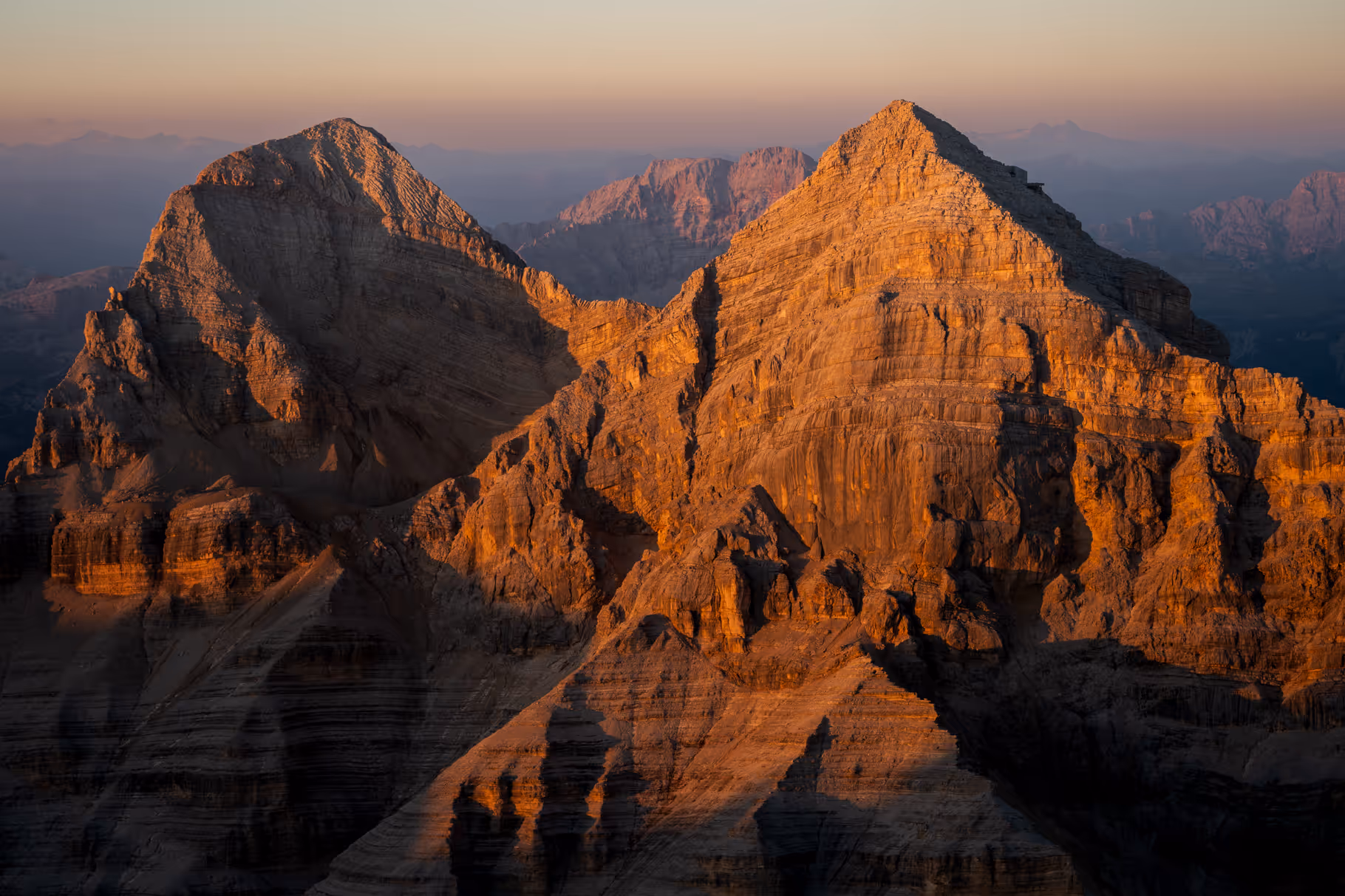 Sunlit rugged mountain peaks with layers of rock and shadows at sunset.