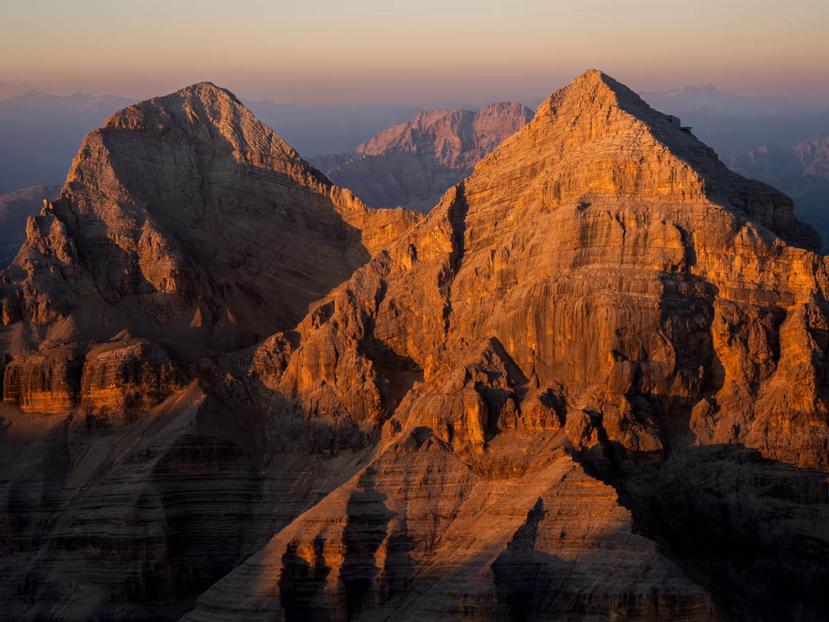 Sunset-lit rugged mountain peaks with sharp ridges and valleys under a clear sky.