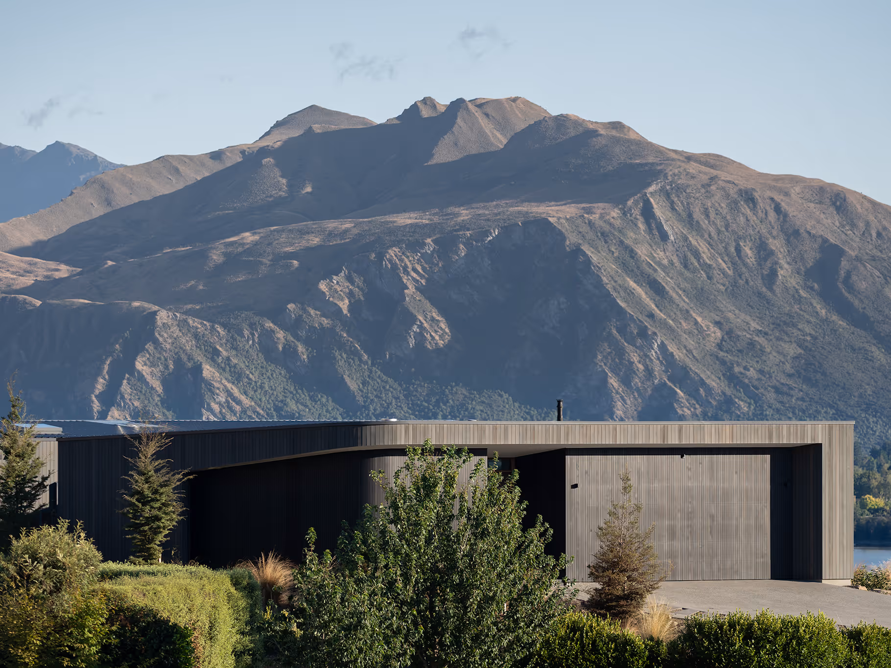Modern rectangular house with vertical siding in front of large mountainous landscape under clear sky.