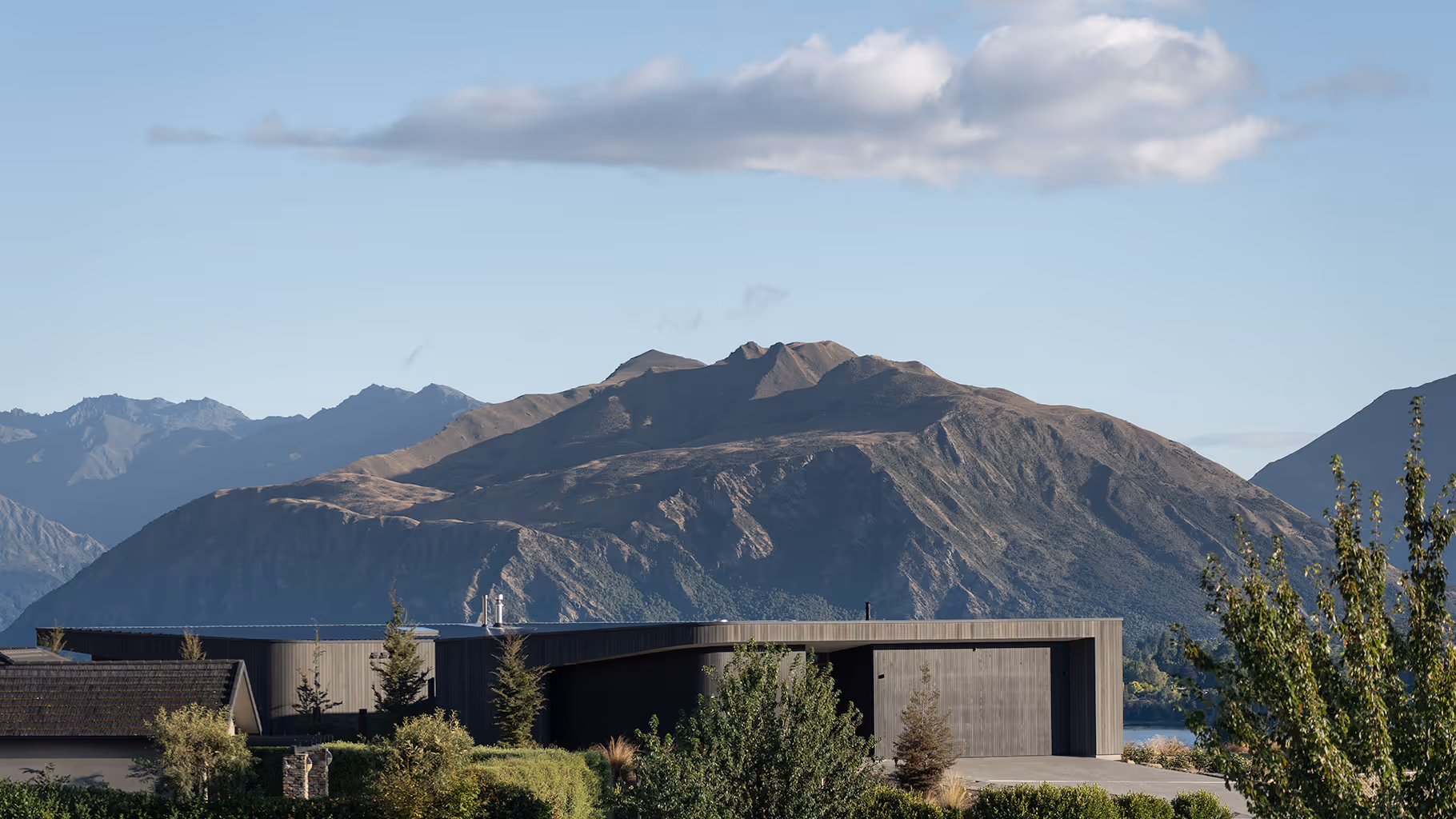 Modern house surrounded by trees with a large mountain and clear sky in the background.