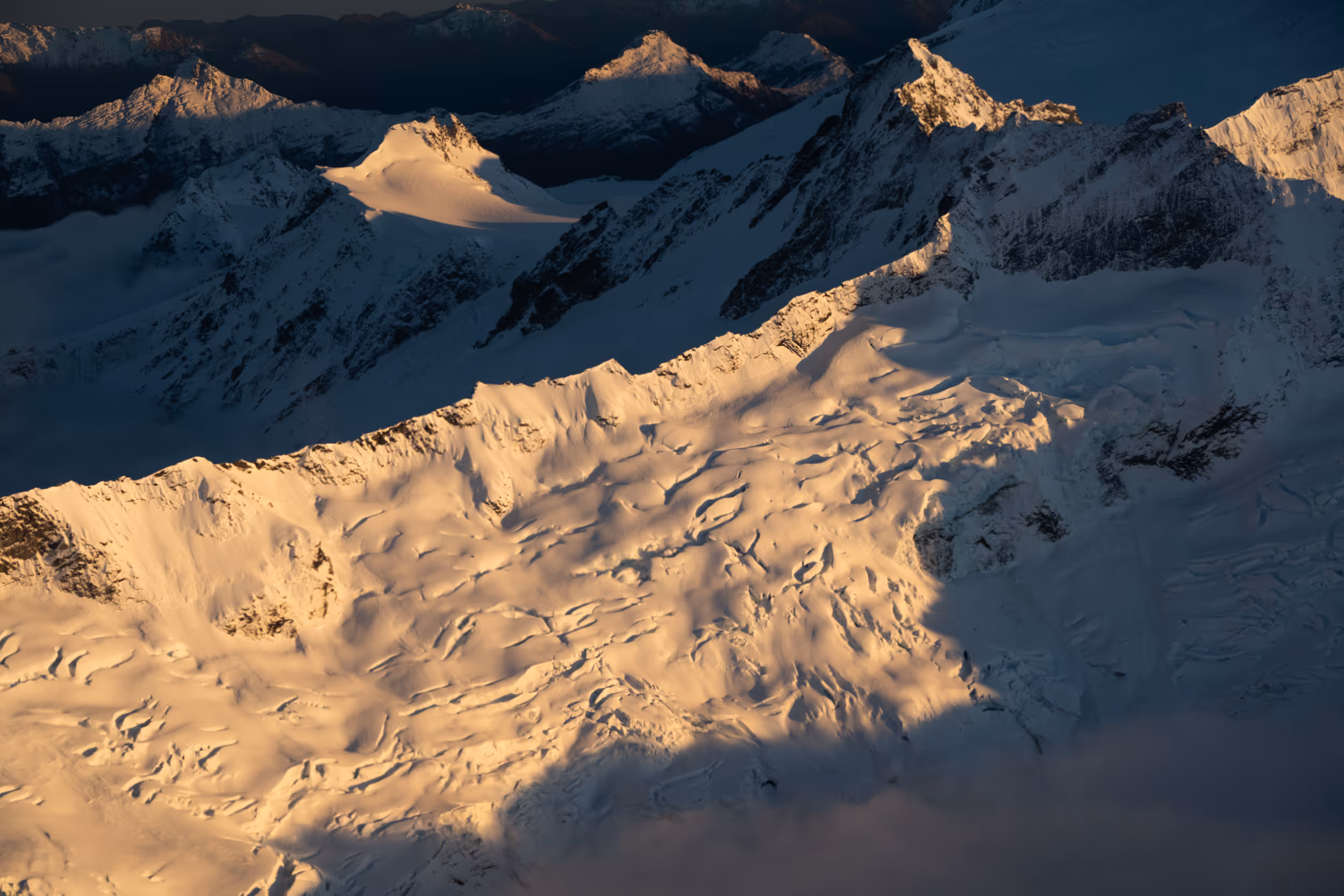 Snow-covered mountain peaks illuminated by warm sunlight with shadows in the valleys.
