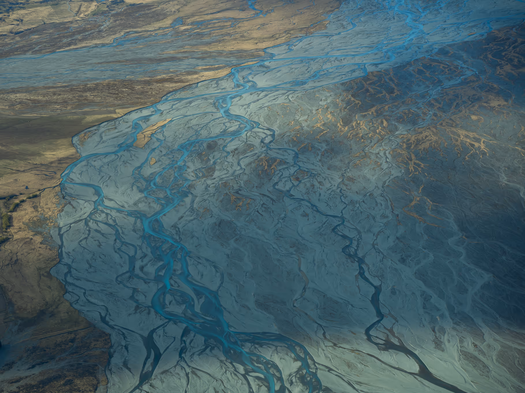 Aerial view of winding blue rivers flowing through a textured landscape of sand and mud flats.