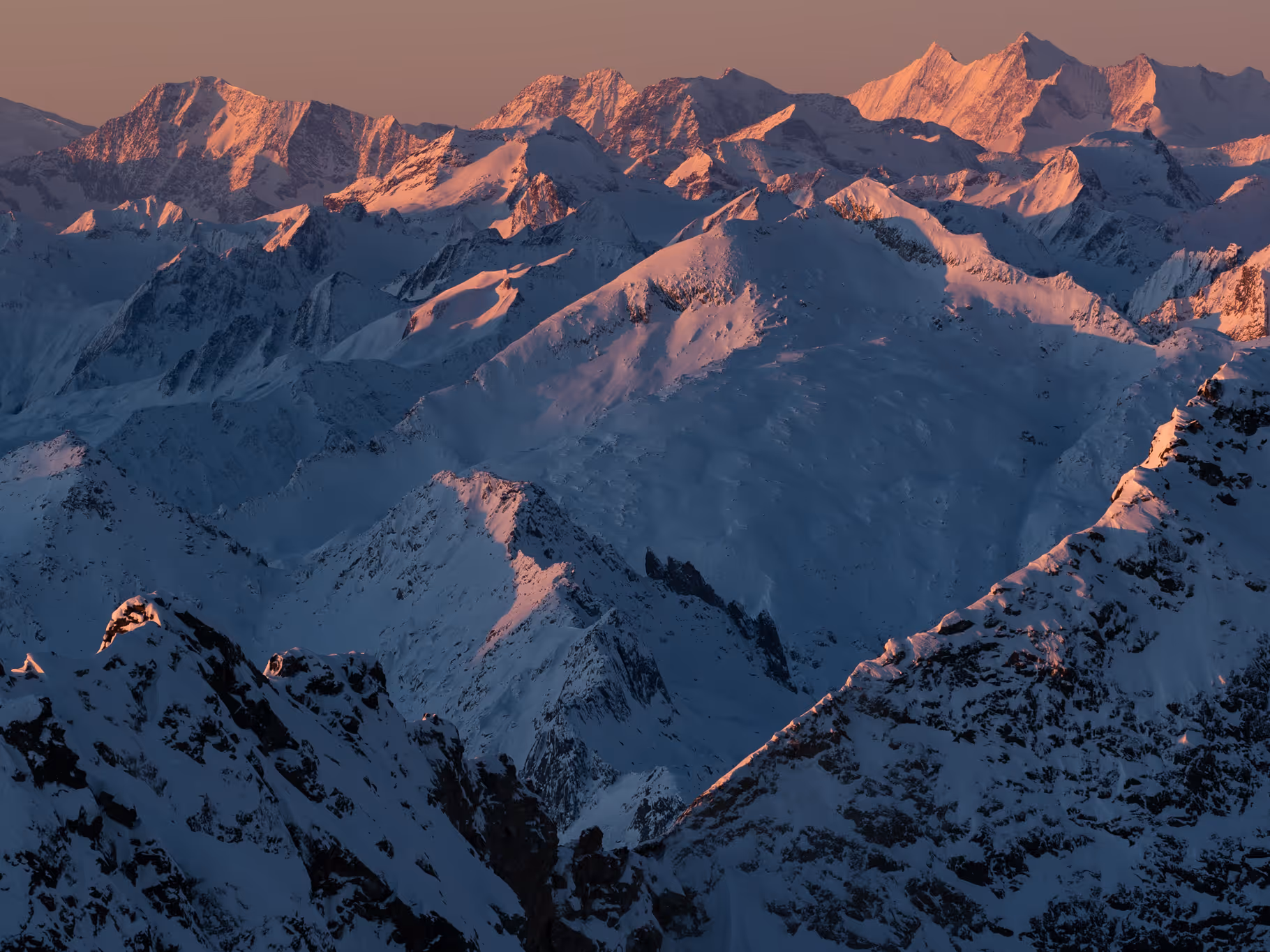 Snow-covered mountain peaks illuminated by warm sunlight during sunrise or sunset.