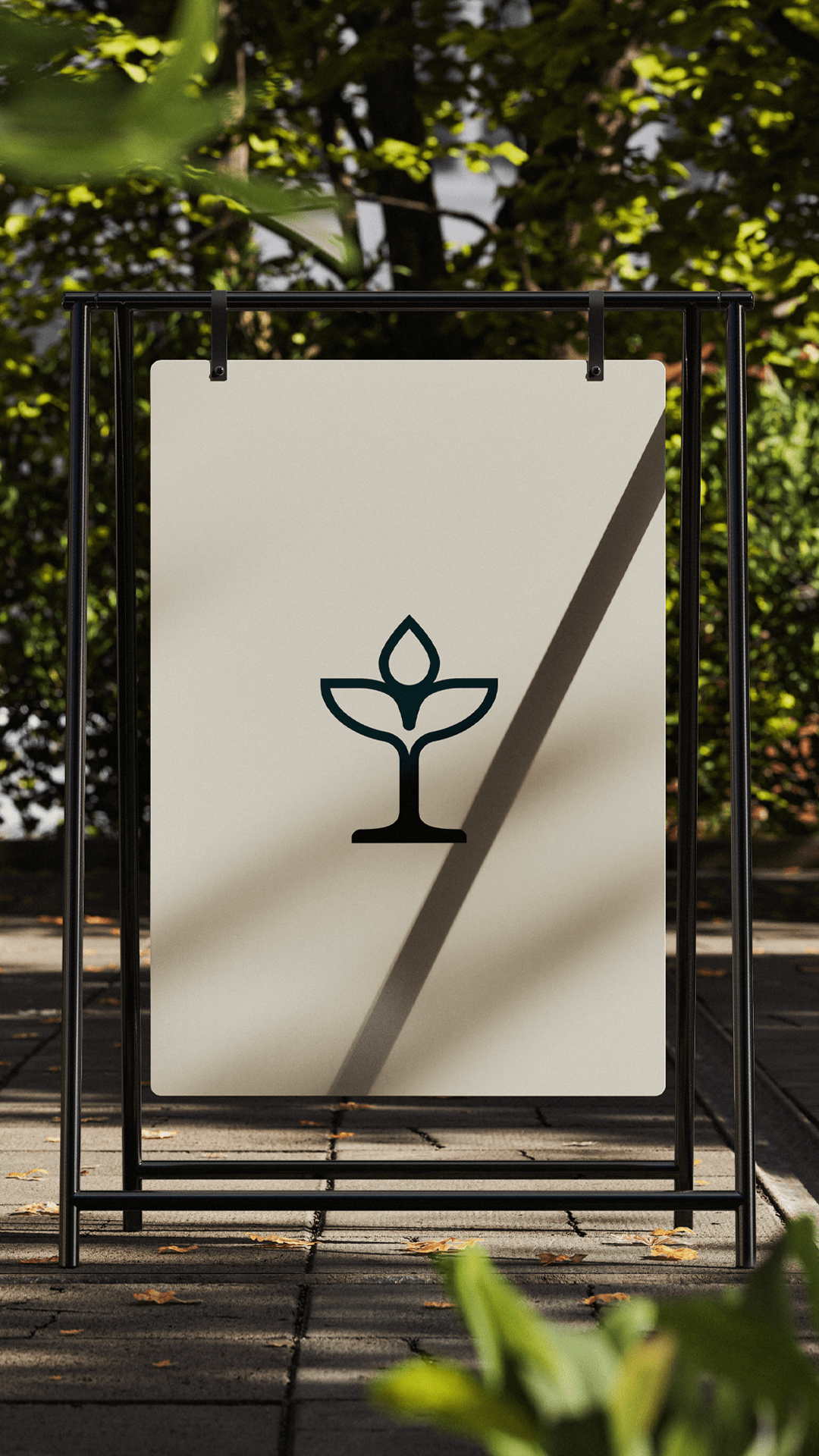 Outdoor beige sign with a black minimalist plant logo hanging on a black metal frame, with trees and sunlight in the background.