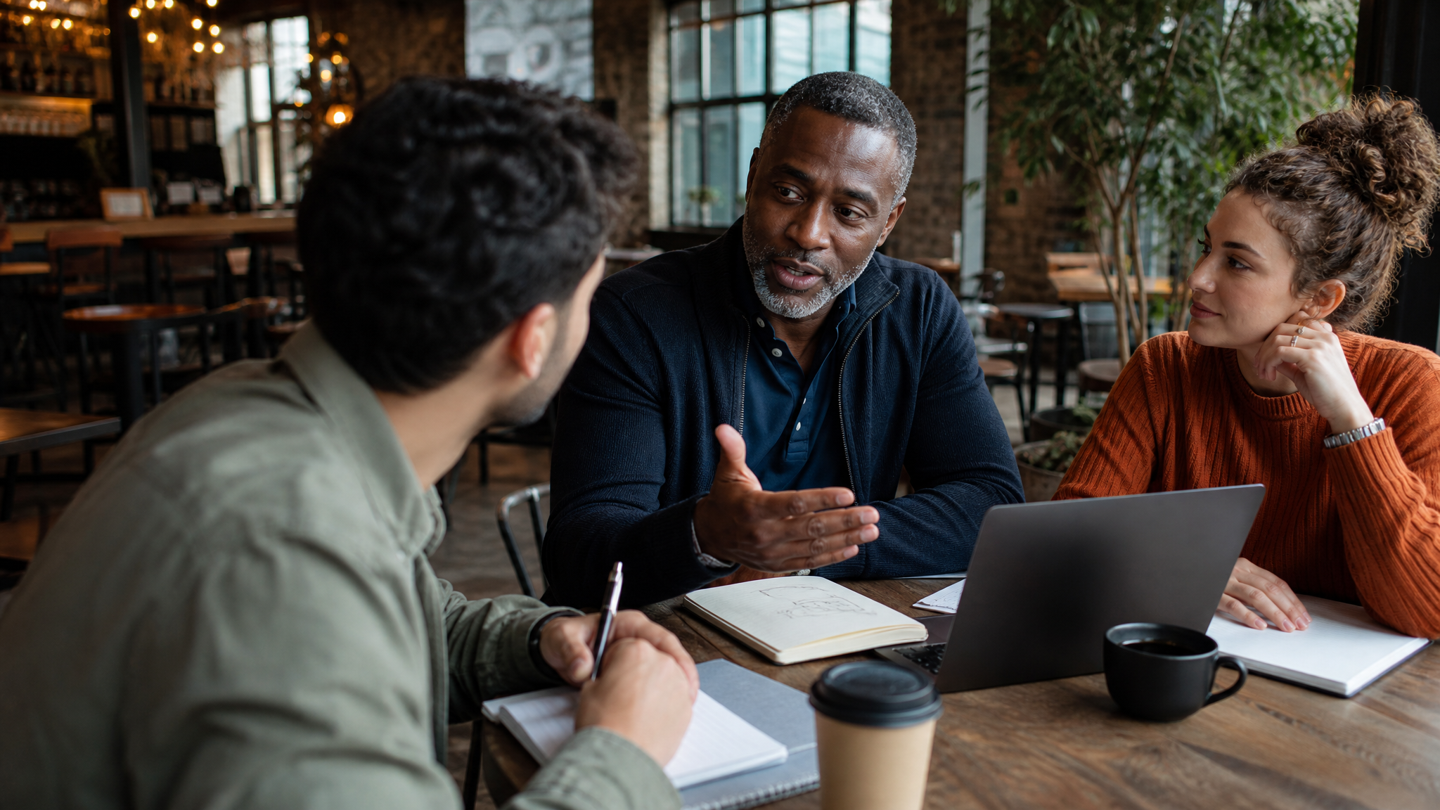 A mentor talking with two students over coffee and a laptop