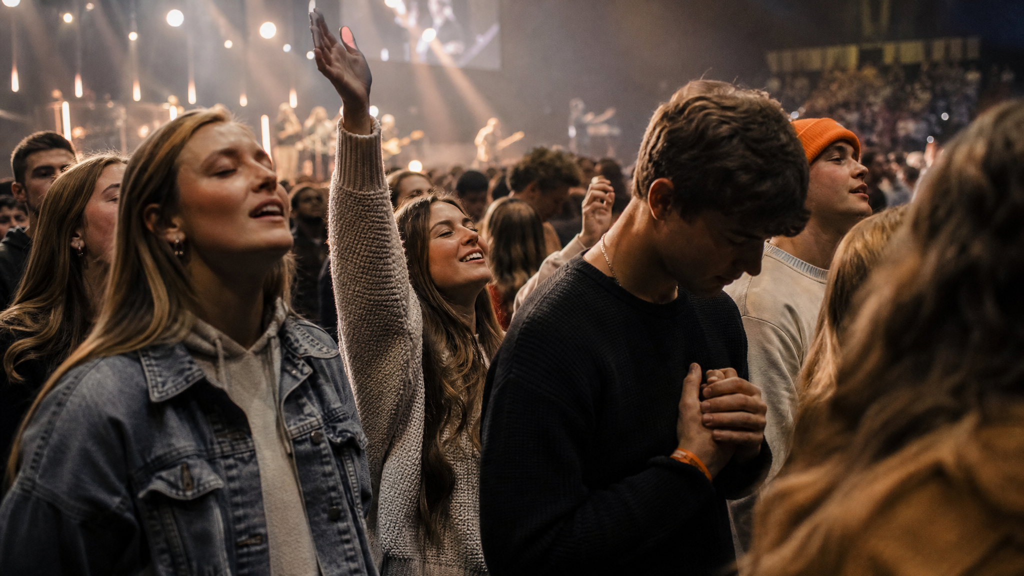 Students worshiping in a crowded room with hands raised