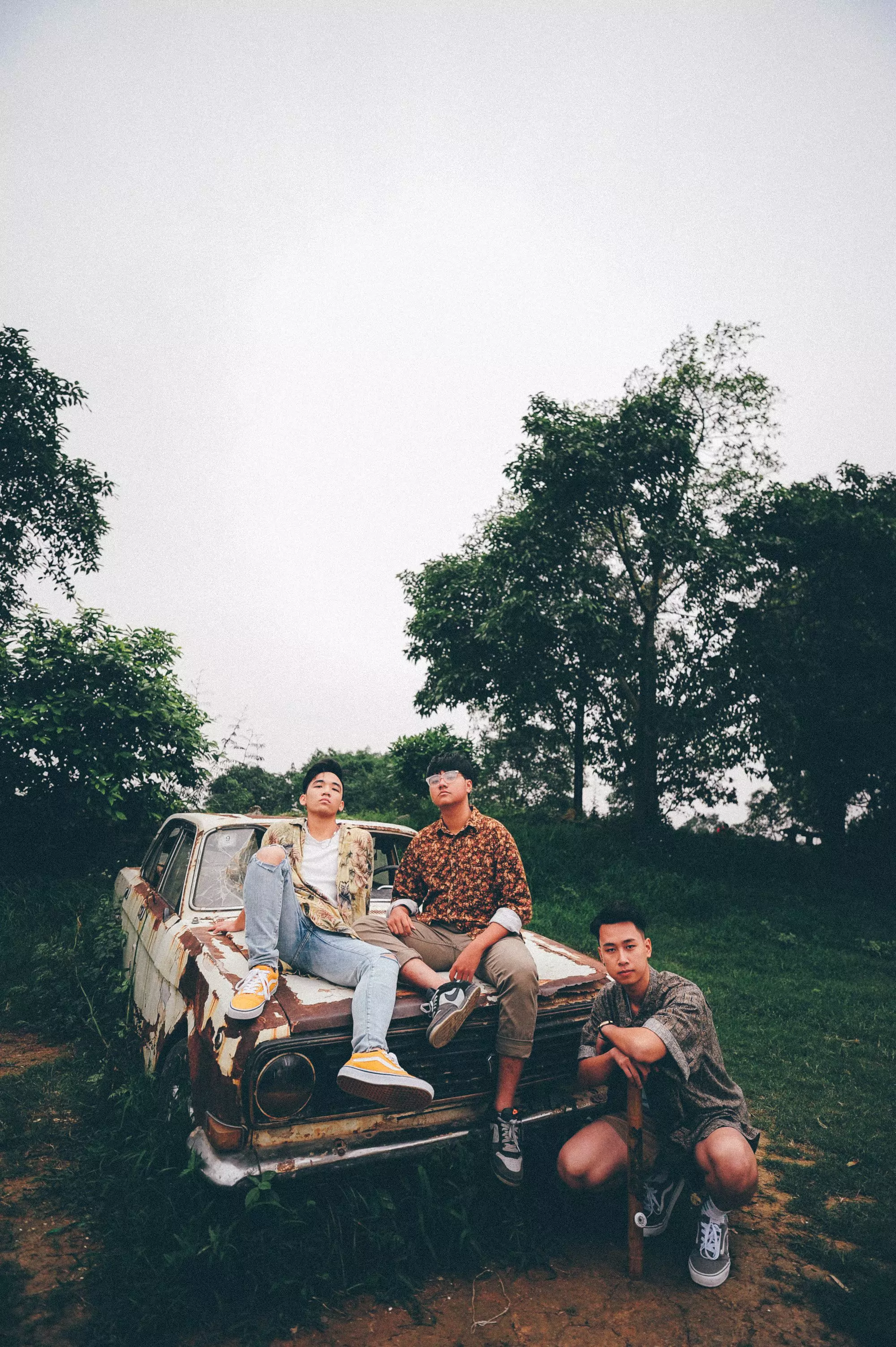 man kneeling beside wrecked car with two men sitting on hoodby Donald Tran