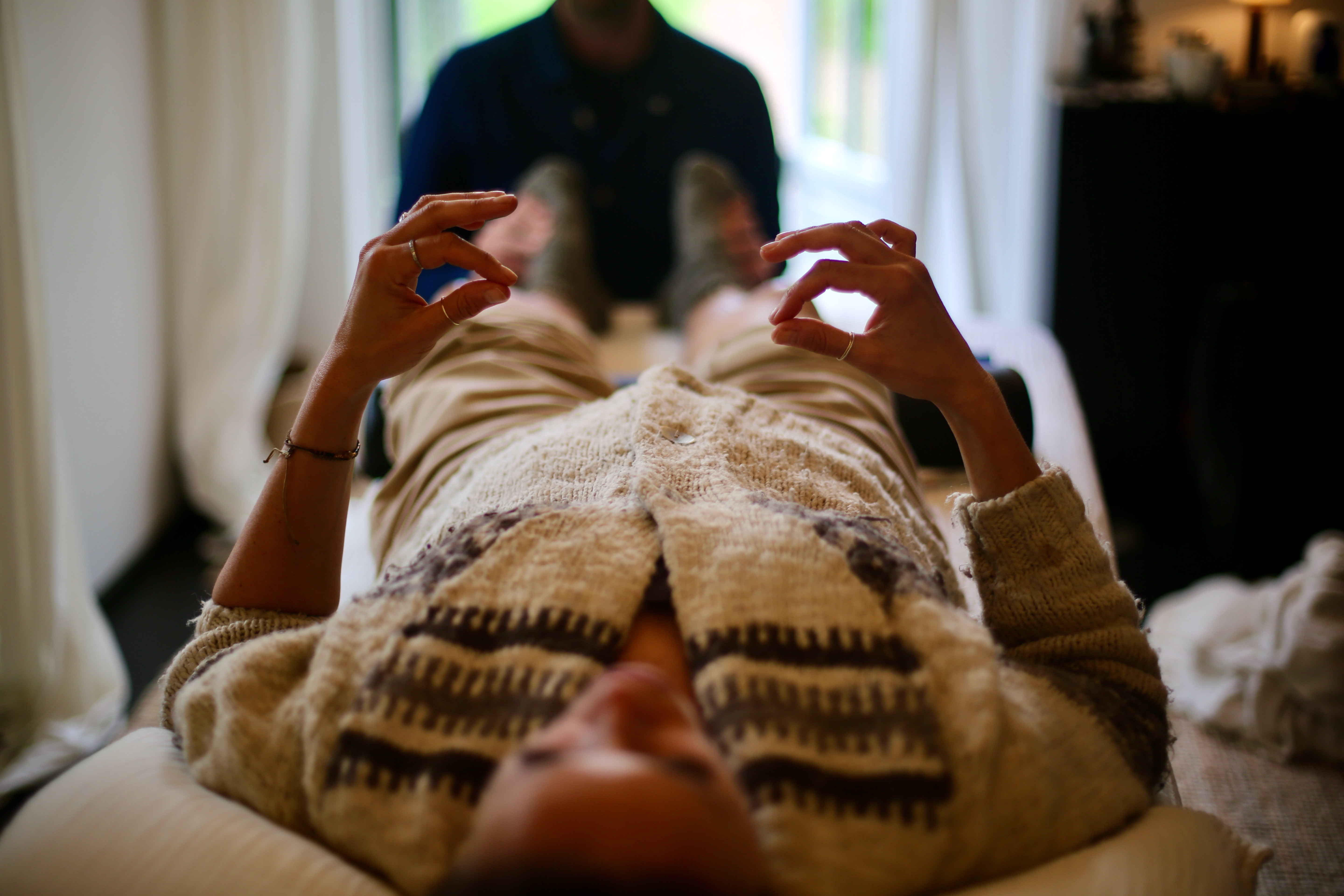 Man with glasses talks while a person lies on a massage table covered by a beige blanket.
