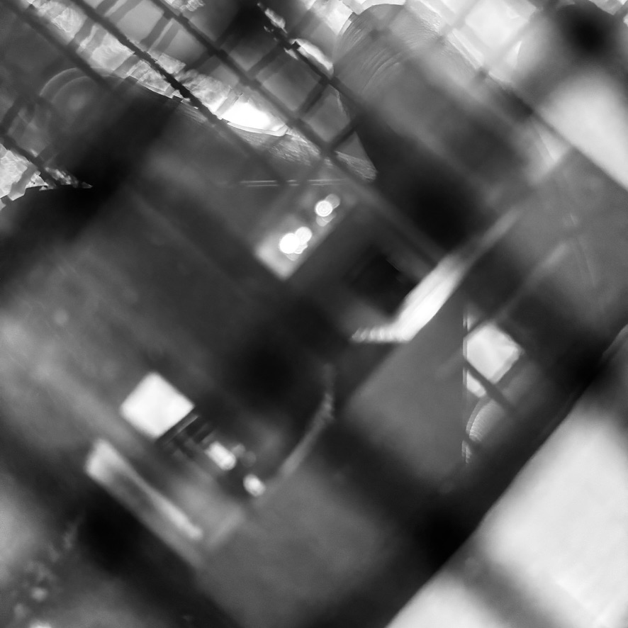 Black and white abstract image showing blurred grid-like patterns with light and shadow creating a complex layered effect.