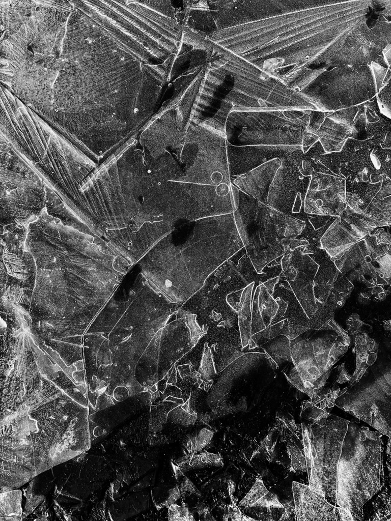 Close-up of cracked, shattered ice with intricate geometric patterns and varying shades of black and white.