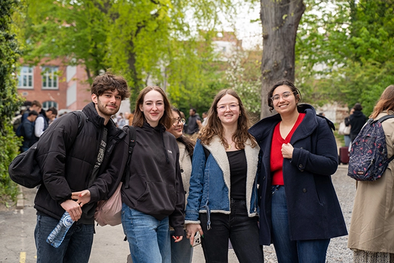 Groupe d'étudiants souriants debout à l'extérieur avec des arbres verts en arrière-plan.