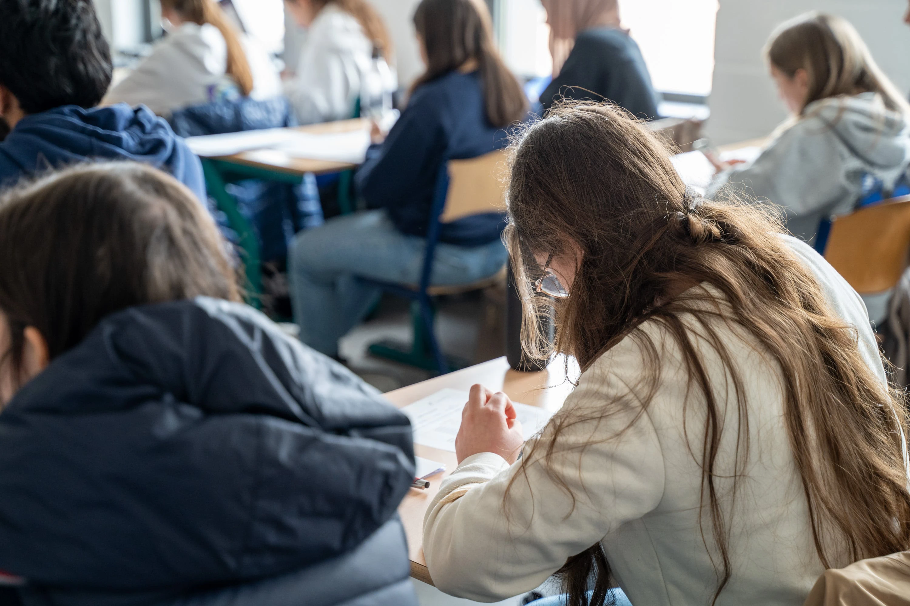 Des élèves dans une salle de classe concentrés sur un devoir écrit au bureau.