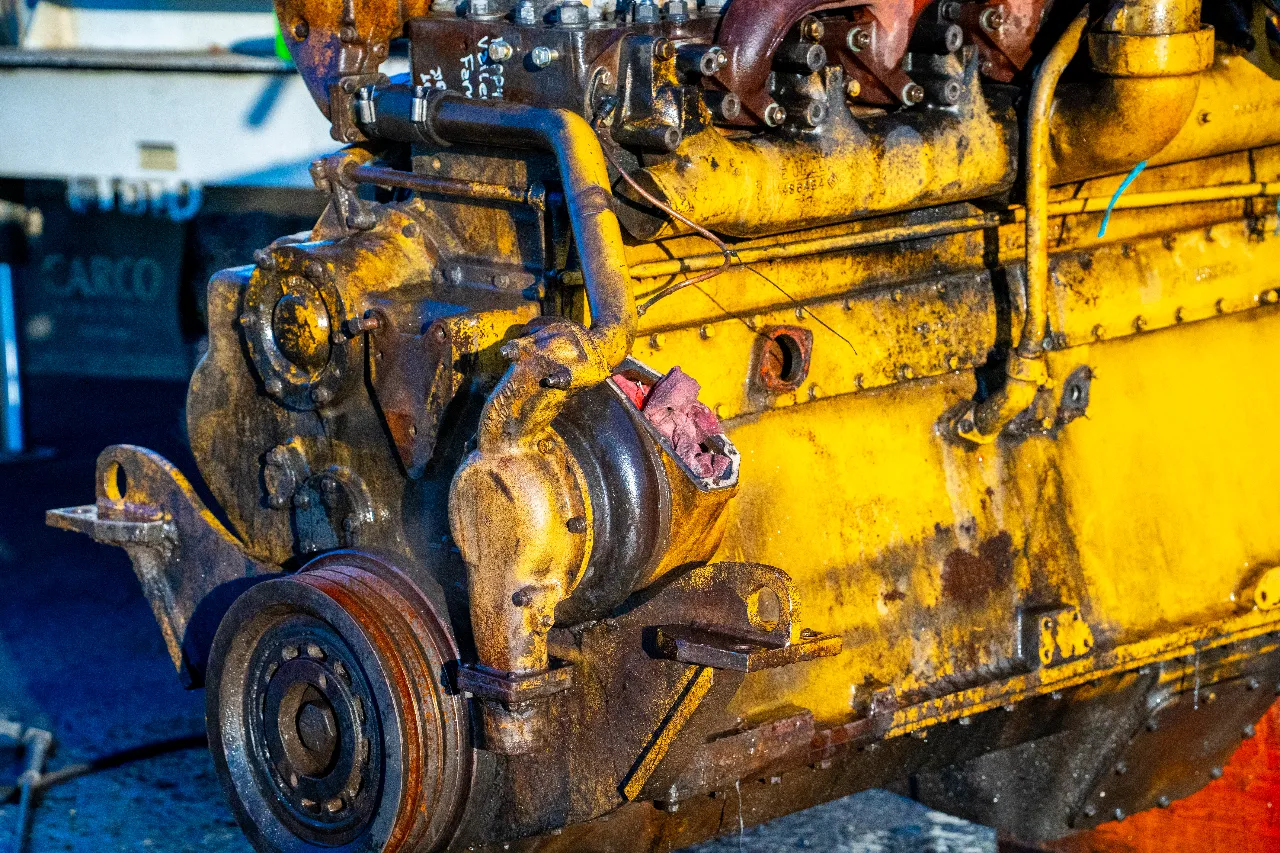 Yellow diesel block with worn pulley and hoses staged for heavy-duty engine repair; visible text reads “AXCO.”