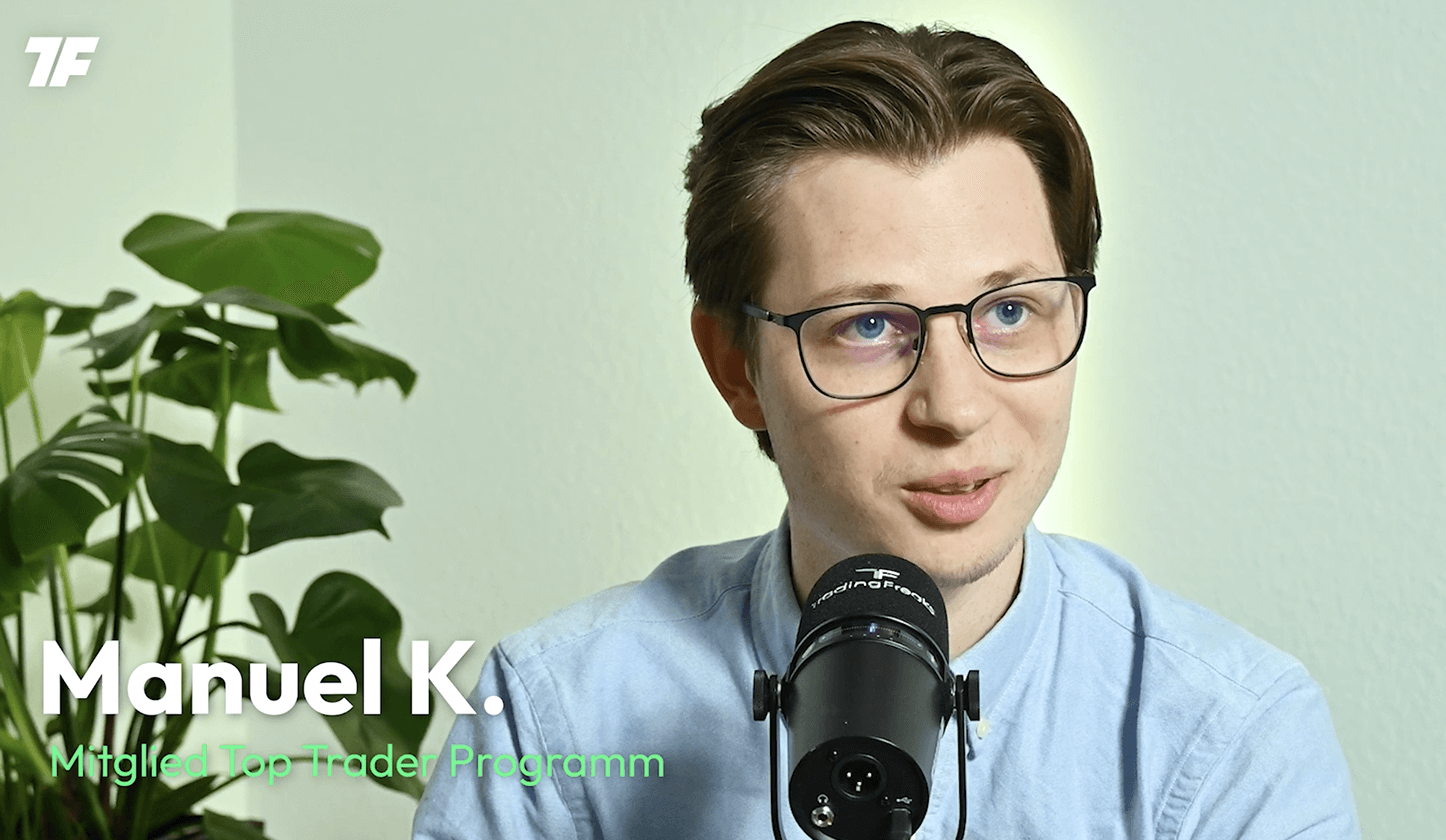 Mann mit Brille spricht in ein Mikrofon vor einer hellen Wand; Top Trader Programm-Text links.