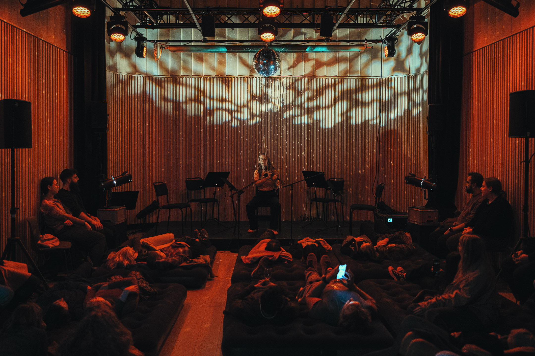 Person som spiller fiolin på en scene under en discokule.